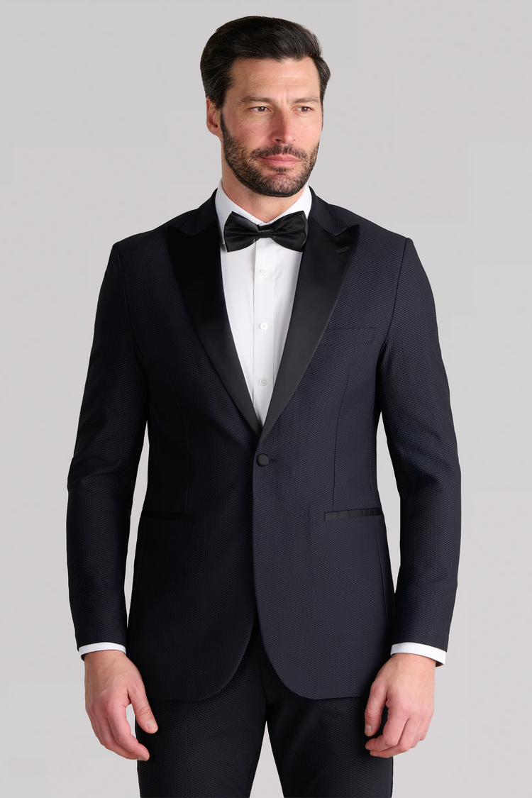 A man with short dark hair and a beard wears the Twillory AIR Tuxedo Blazer in black, featuring a breathable design and satin peaked lapel, paired with a white shirt and black bow tie. He stands against a light gray background, looking slightly to the side. A man with short dark hair and a beard wears the Twillory AIR Tuxedo Blazer in black, featuring a breathable design and satin peaked lapel, paired with a white shirt and black bow tie. He stands against a light gray background, looking slightly to the side.