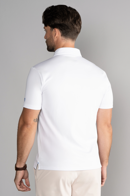 A man with neatly styled dark hair wears the Twillory Short Sleeve Polo Solid in White and light beige pants, accessorized with a watch on his left wrist. He faces away from the camera against a plain light gray background.