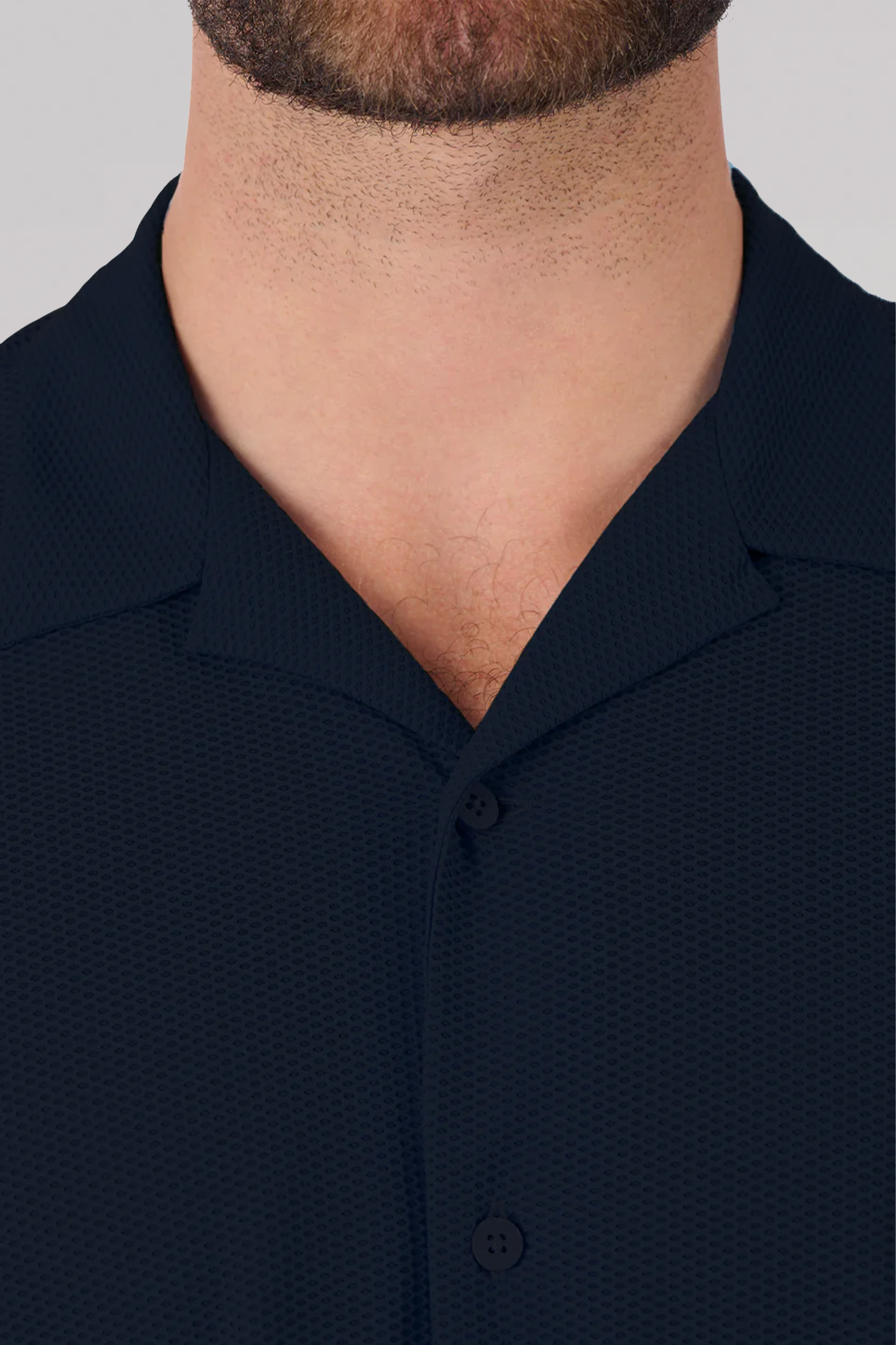 A close-up of a man's neck and upper chest wearing the Twillory AIR Resort Shirt Solid // Black. Made from cooling 4-way stretch AIR fabric, the shirt features black buttons, a relaxed camp collar, and his lower face with beard stubble is visible.