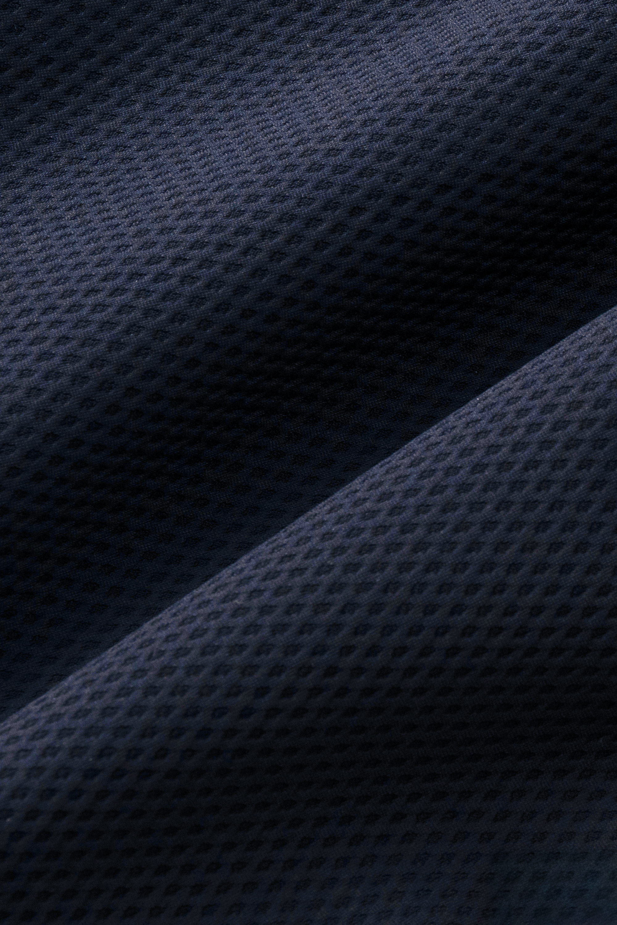 Close-up of Twillory’s AIR Zip Polo Solid in Navy, featuring dark blue 360° Airflow Fabric with a repeating diamond pattern. Light and shadow emphasize the hyper-breathable, three-dimensional texture of this soft performance polo.