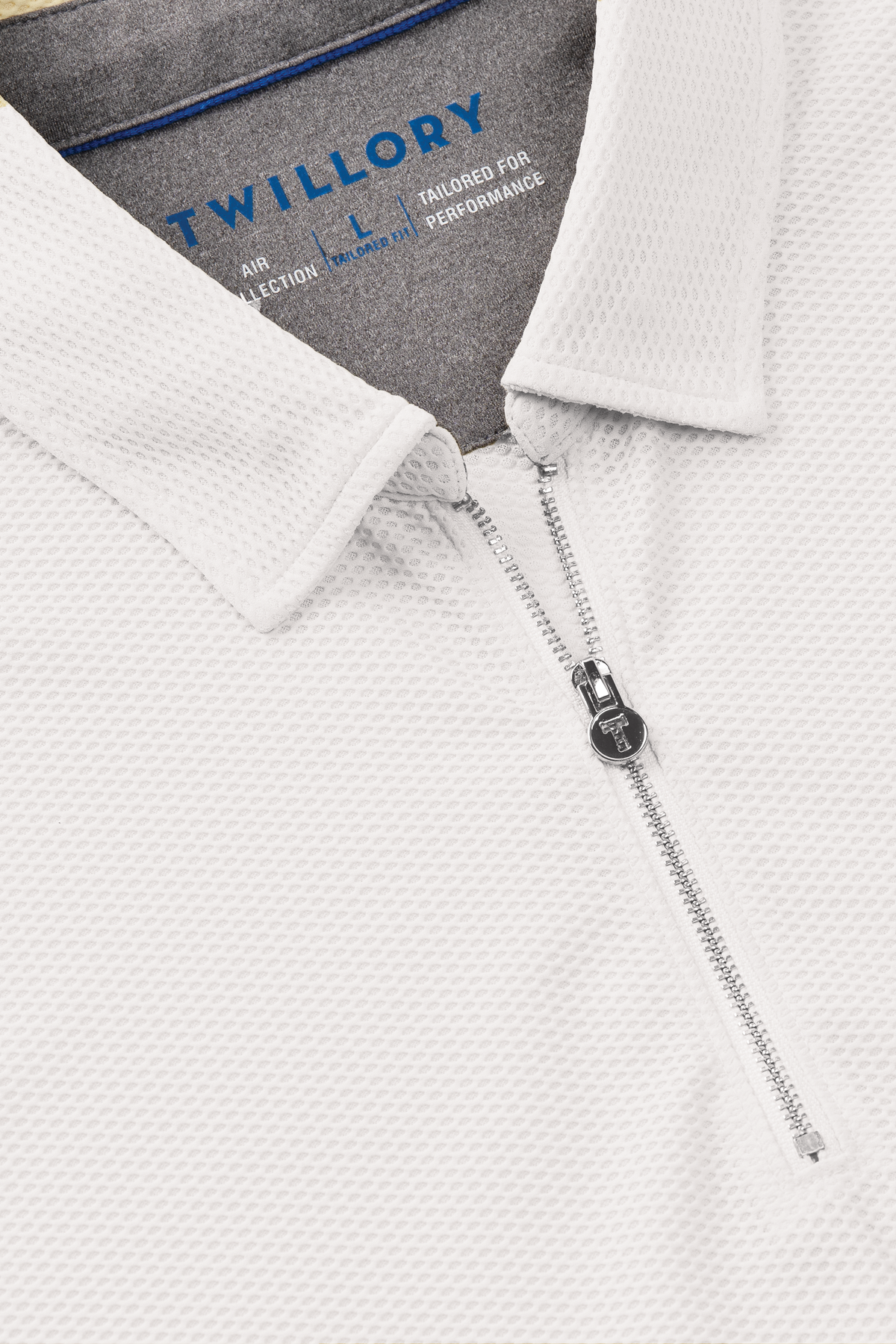 Close-up of the Twillory AIR Zip Polo Solid in white, featuring hyper-breathable 360° Airflow Fabric, a quarter-zip front with silver pull tab, and a flat spread collar. Inside, blue print reads: “Twillory tailored for performance.”.