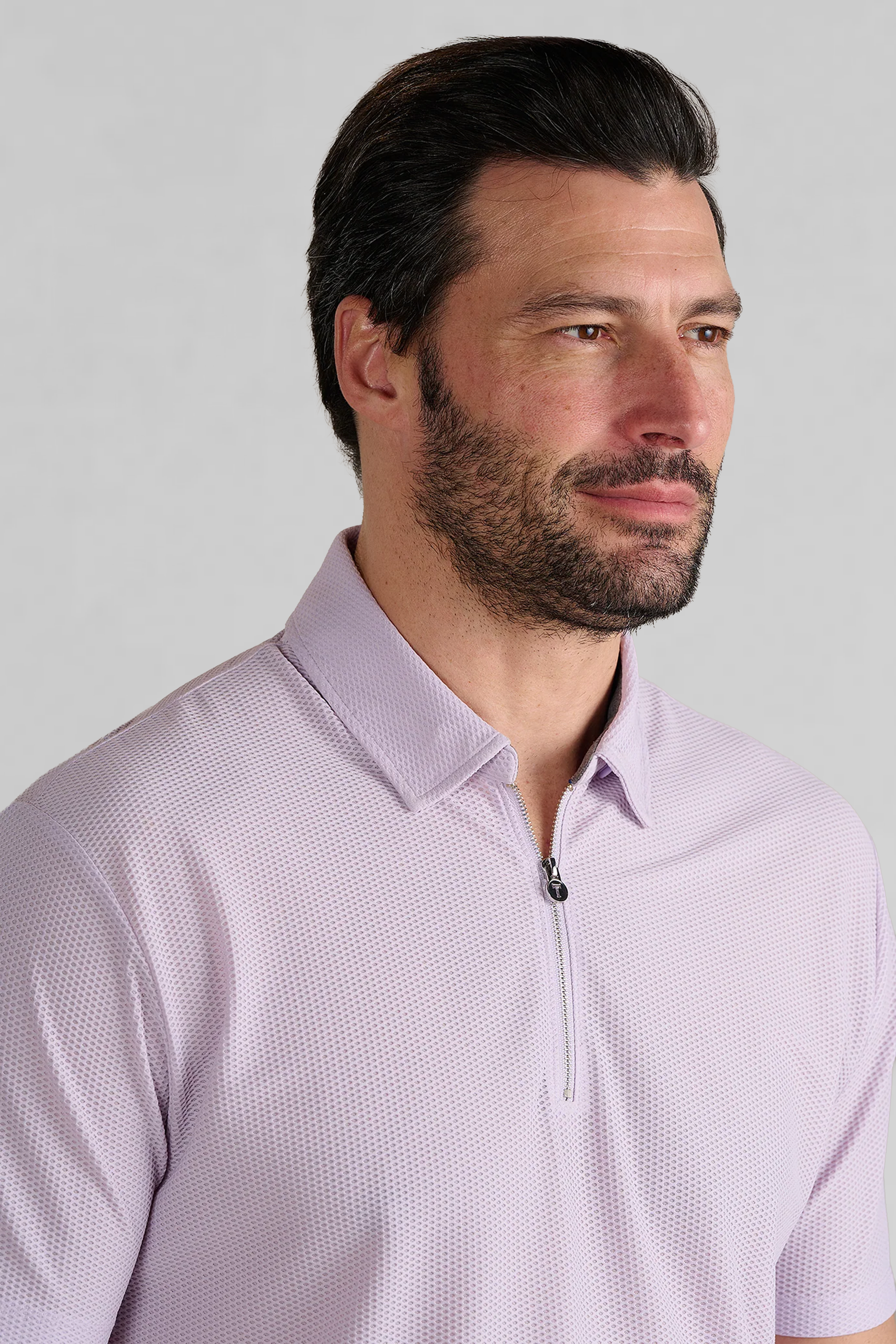 A man with short dark hair and a beard is wearing the Twillory AIR Zip Polo Solid in Lilac. He looks slightly to the left with a neutral expression against a plain, light gray background.