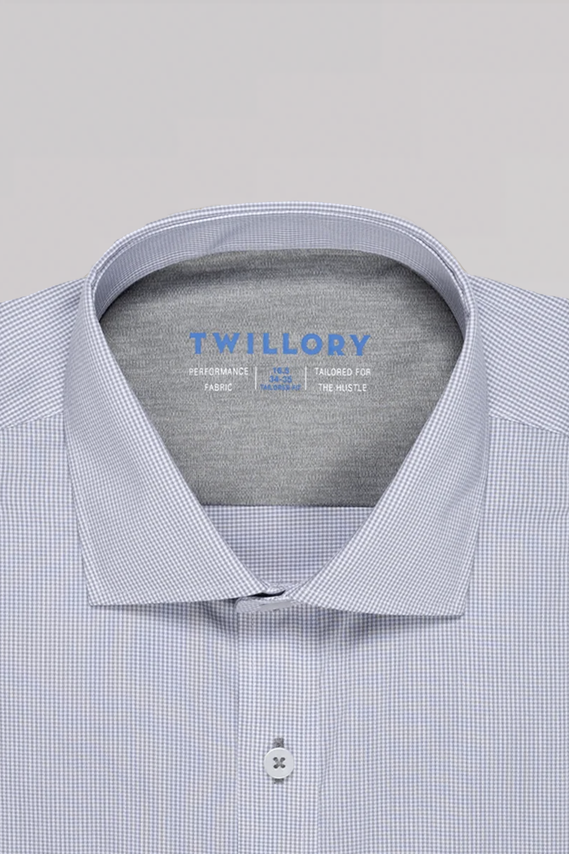 A close-up of the Twillory ADVANCER // Performance Grey Houndstooth shirt with a spread collar. The non-iron performance shirt features product details in blue inside the collar, shown neatly buttoned against a plain light gray background.