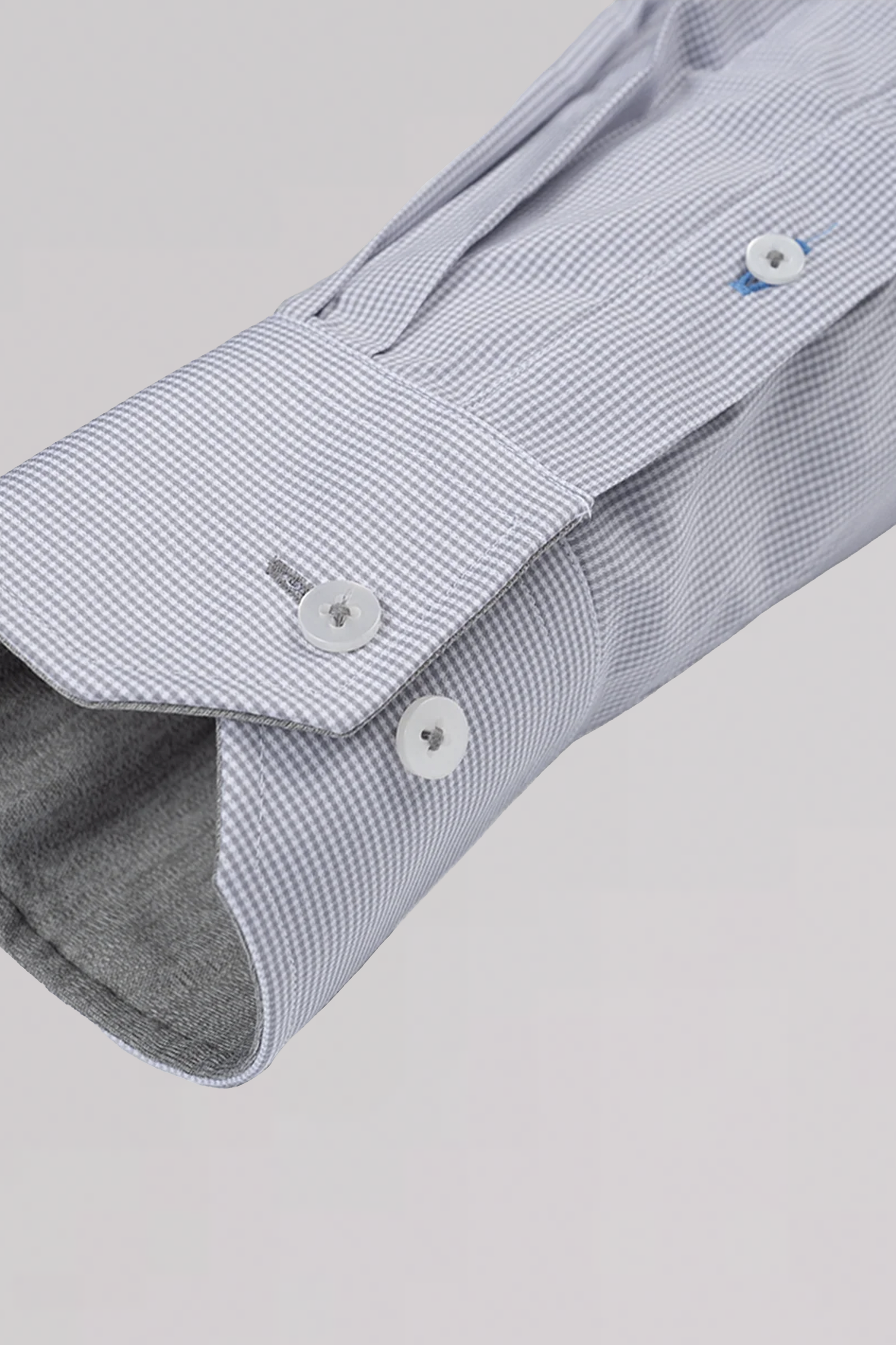 Close-up of the Twillory ADVANCER // Performance Grey Houndstooth shirt sleeve showing its non-iron, textured fabric in light gray houndstooth, with a structured cuff featuring two white buttons and a small blue button on the placket.