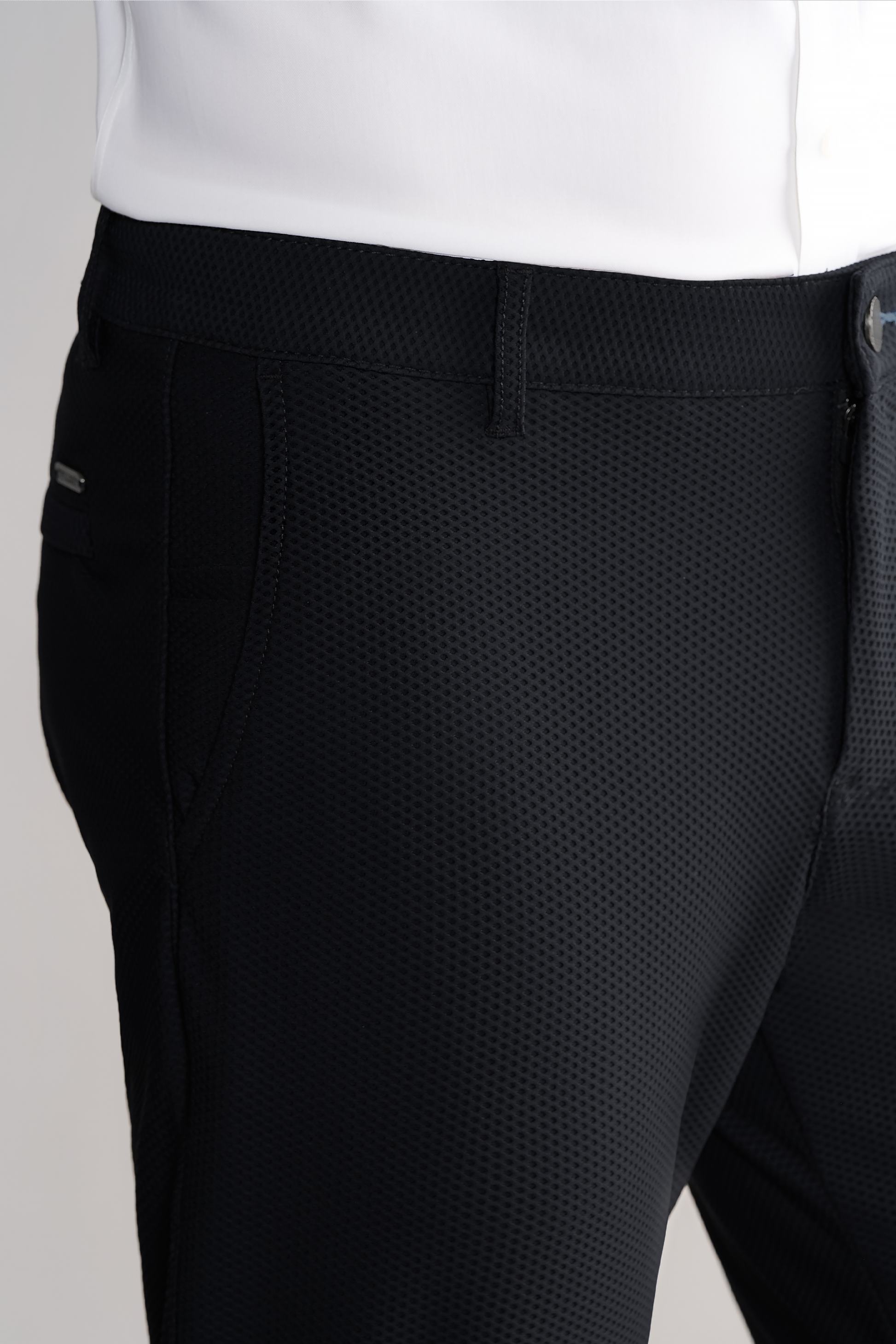 A close-up shows a person wearing Twillory AIR Pants // Heather Charcoal and a white shirt, focusing on the waist, upper thigh, side pocket, belt loop, fly detail, and the pants’ subtle checkered pattern.