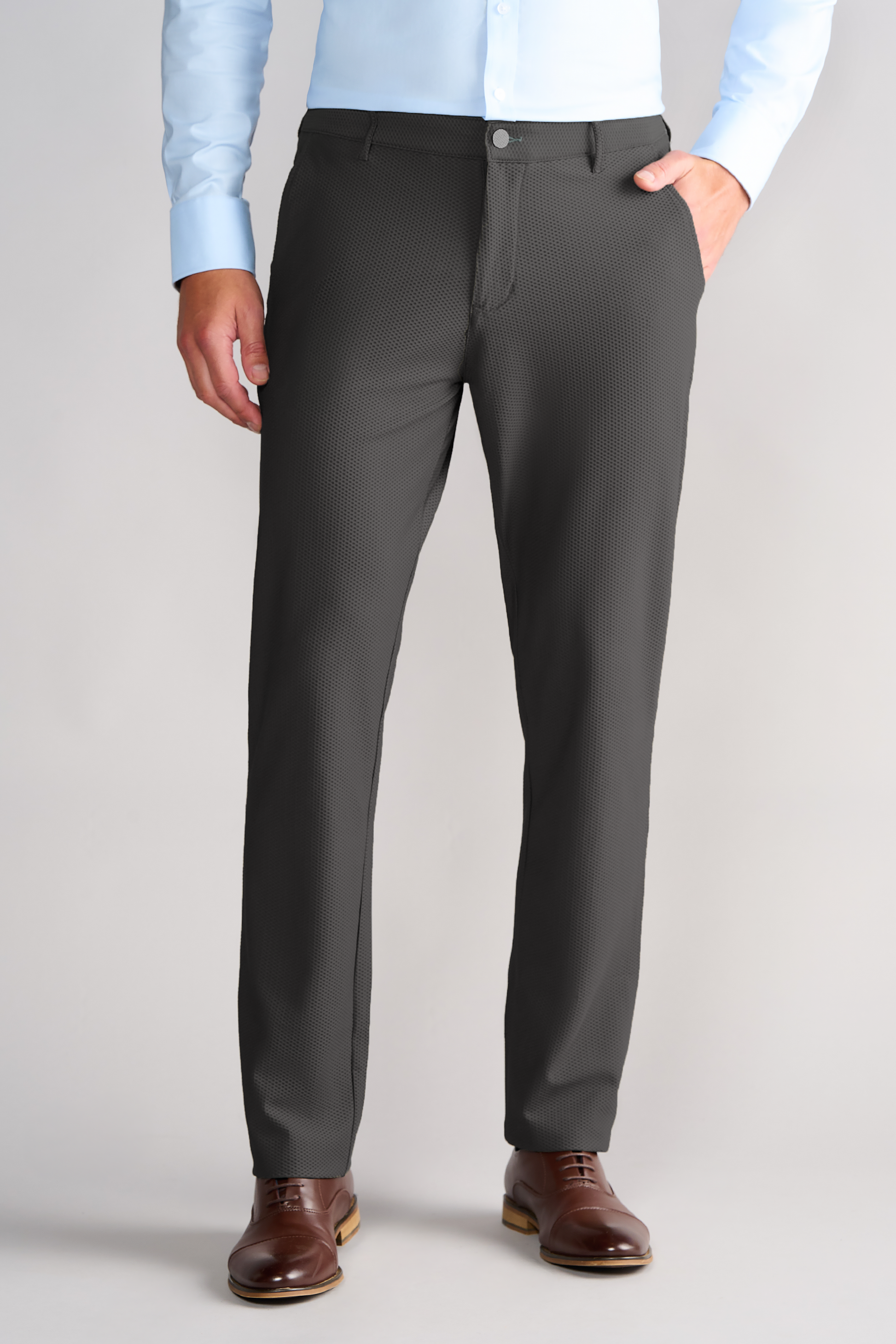 A man stands facing forward in Twillory AIR Pants in Heather Light Grey, made from moisture-wicking 360° Airflow Fabric. He pairs them with a light blue button-up shirt, brown leather dress shoes, and poses against a plain neutral background.