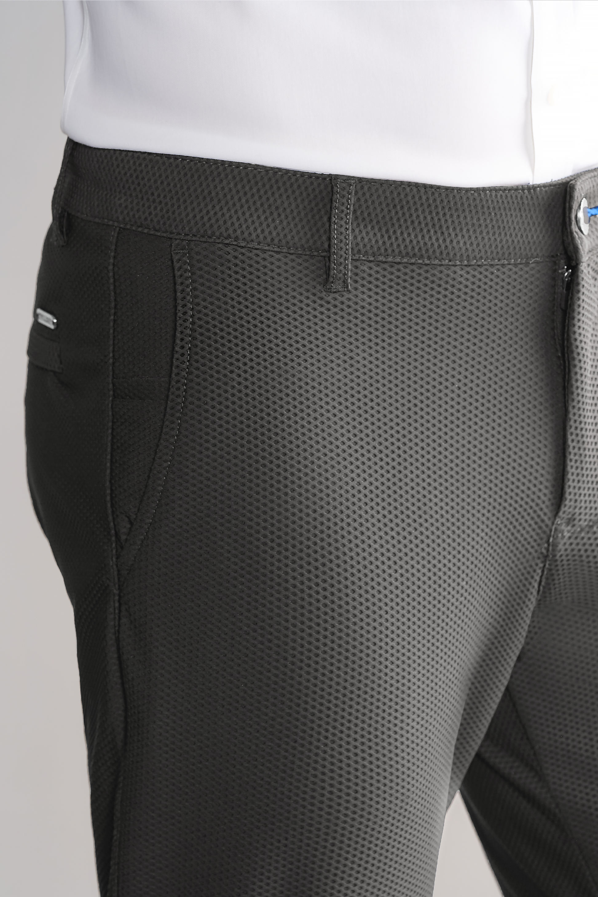 Close-up of a person wearing Twillory AIR Pants // Heather Light Grey, crafted from 360° Airflow Fabric with a fine grid pattern, side pockets, and a visible belt loop. The white shirt is tucked in smoothly against the light background.