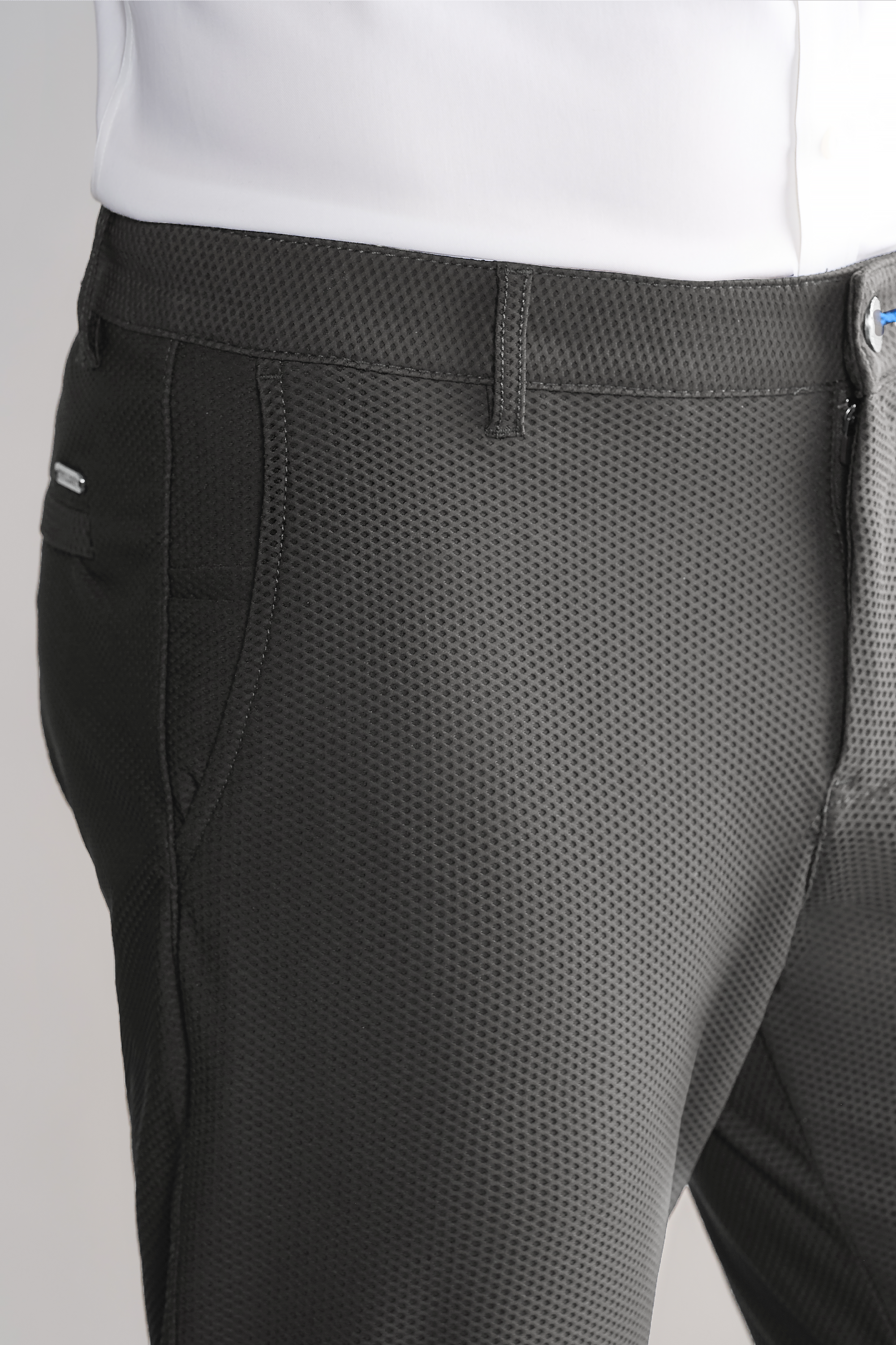 Close-up of a person wearing Twillory AIR Pants // Heather Light Grey, crafted from 360° Airflow Fabric with a fine grid pattern, side pockets, and a visible belt loop. The white shirt is tucked in smoothly against the light background.