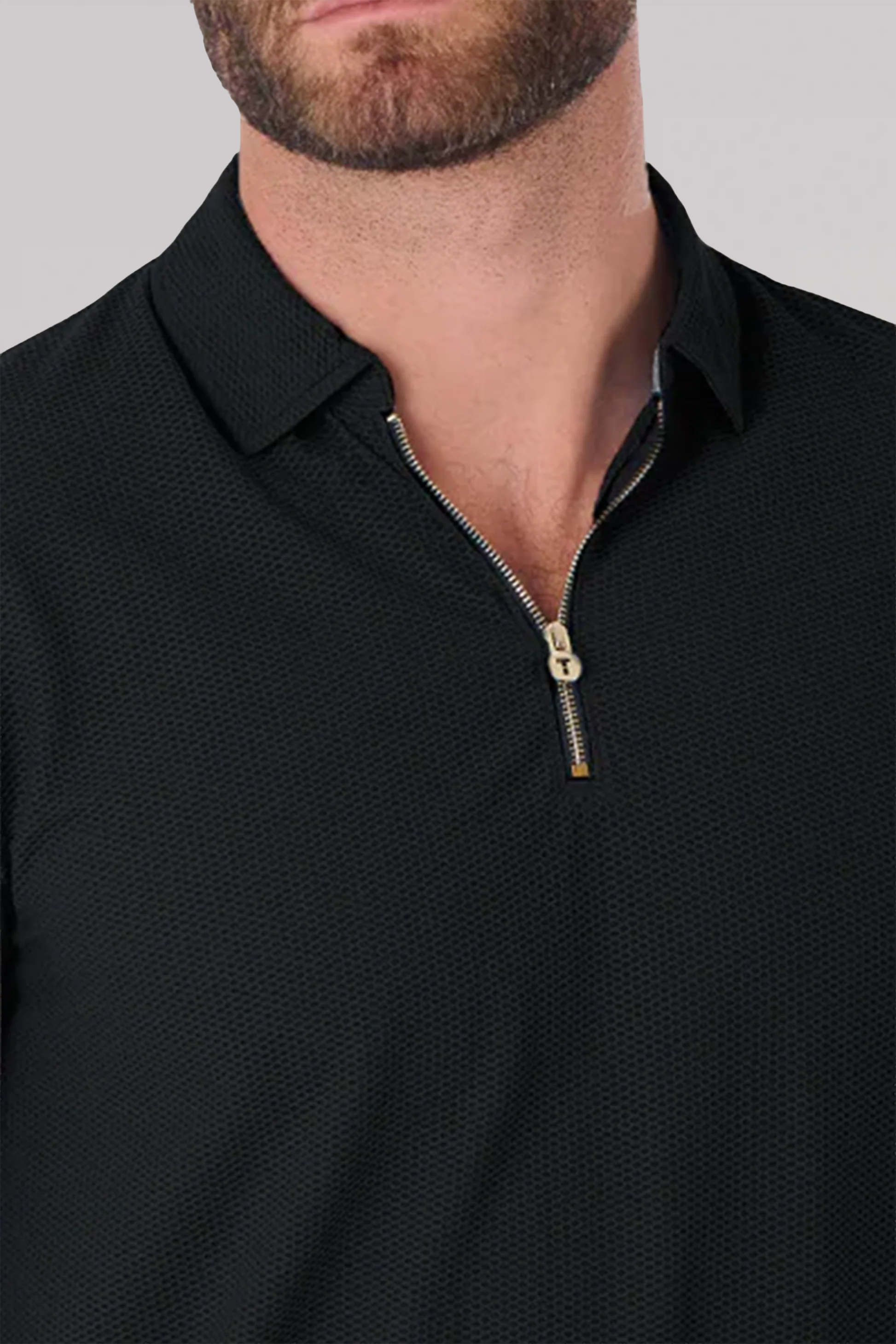 A close-up shows a person wearing Twillory’s AIR Zip Polo Solid // Black, crafted from 360° Airflow Fabric with a short, partially unzipped zipper topped by a metallic pull tab. Only the flat collar, lower face, and upper chest are visible.