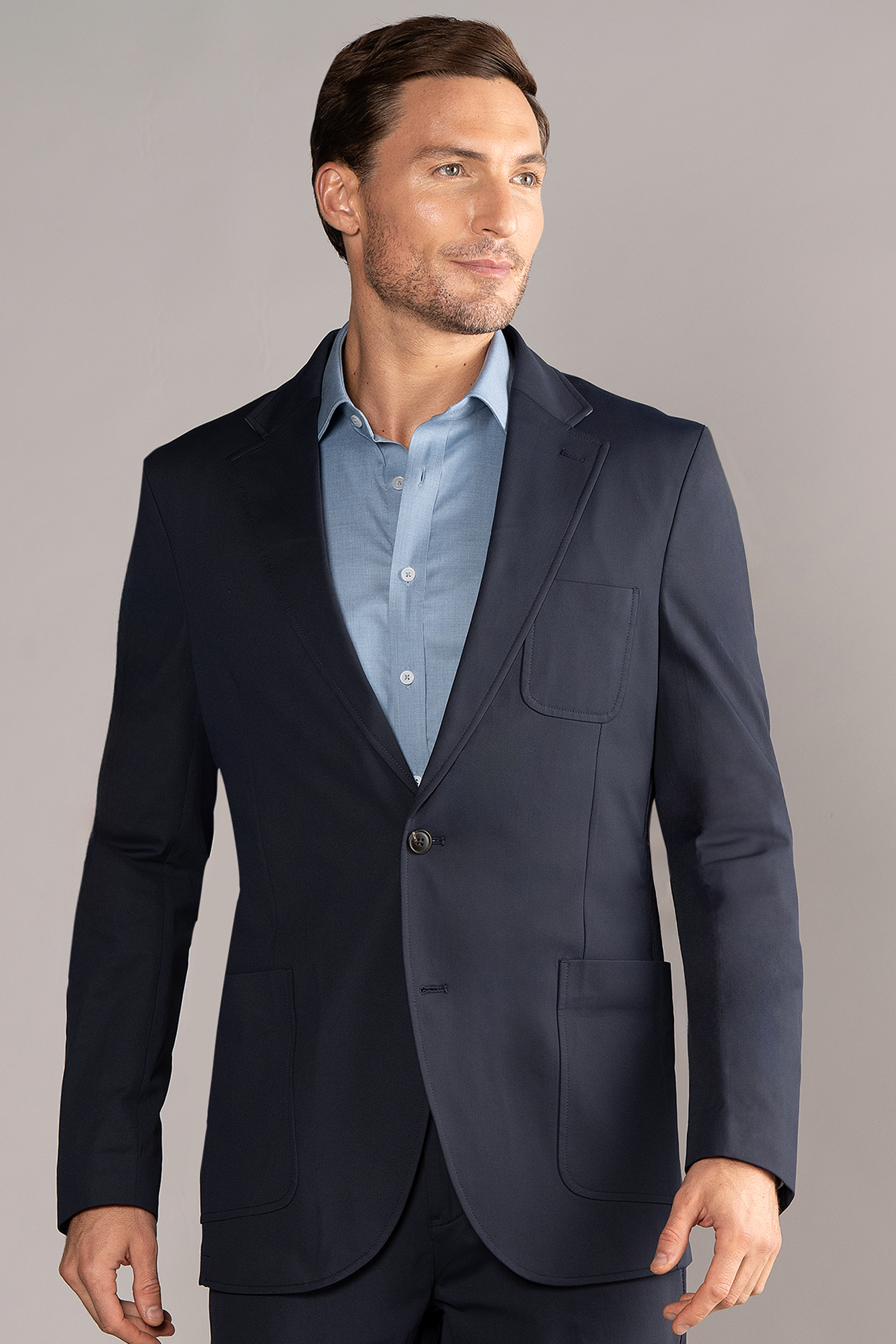 A man with short brown hair and light stubble wears the Twillory Performance Patch Pocket Blazer in navy over a light blue shirt, standing confidently against a light gray background.