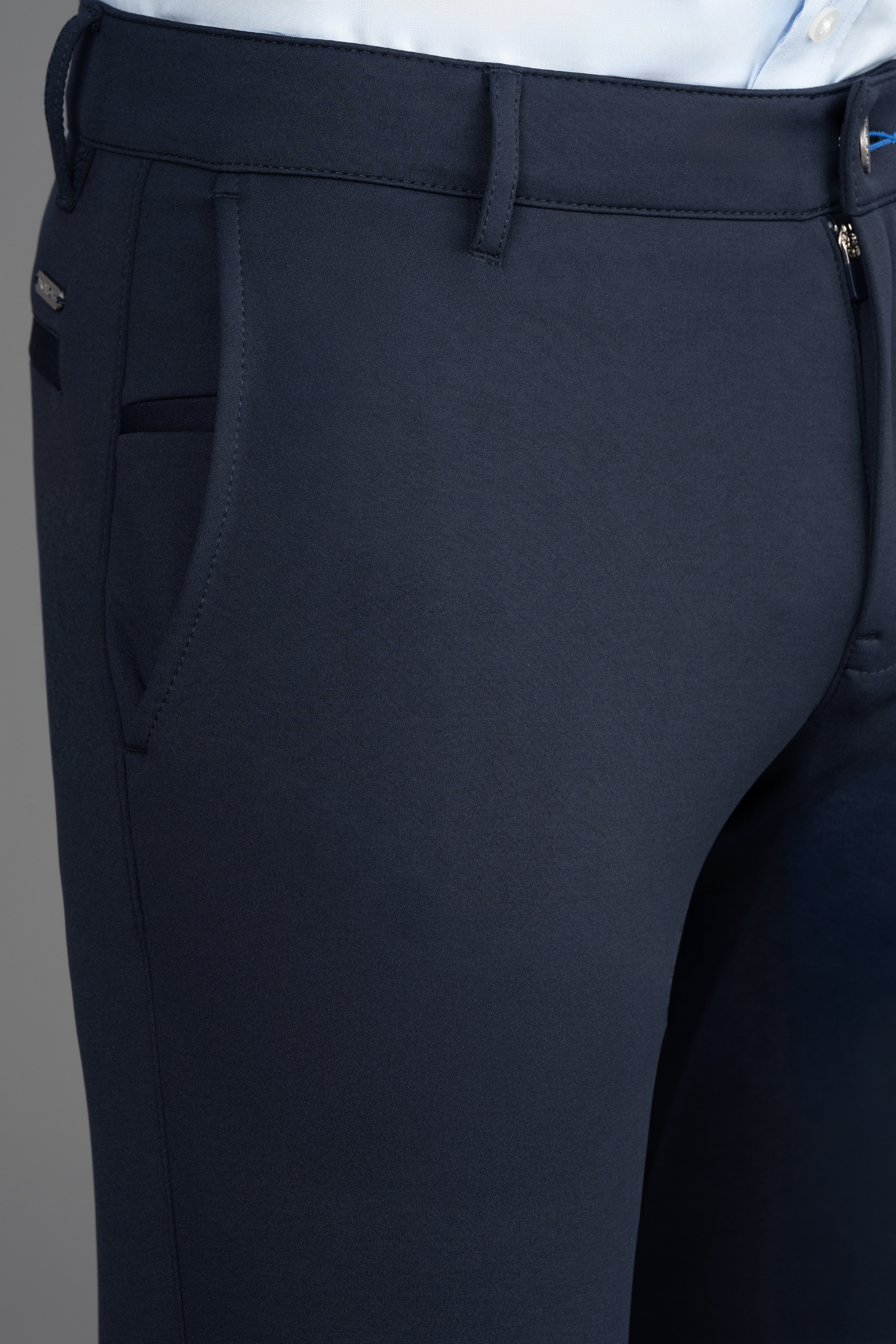 Close-up of a person wearing Twillory Circular Knit Pants // Navy, featuring side pocket, belt loops, wrinkle-resistant 4-way stretch fabric, and a smooth texture. Paired with a tucked-in light blue dress shirt.