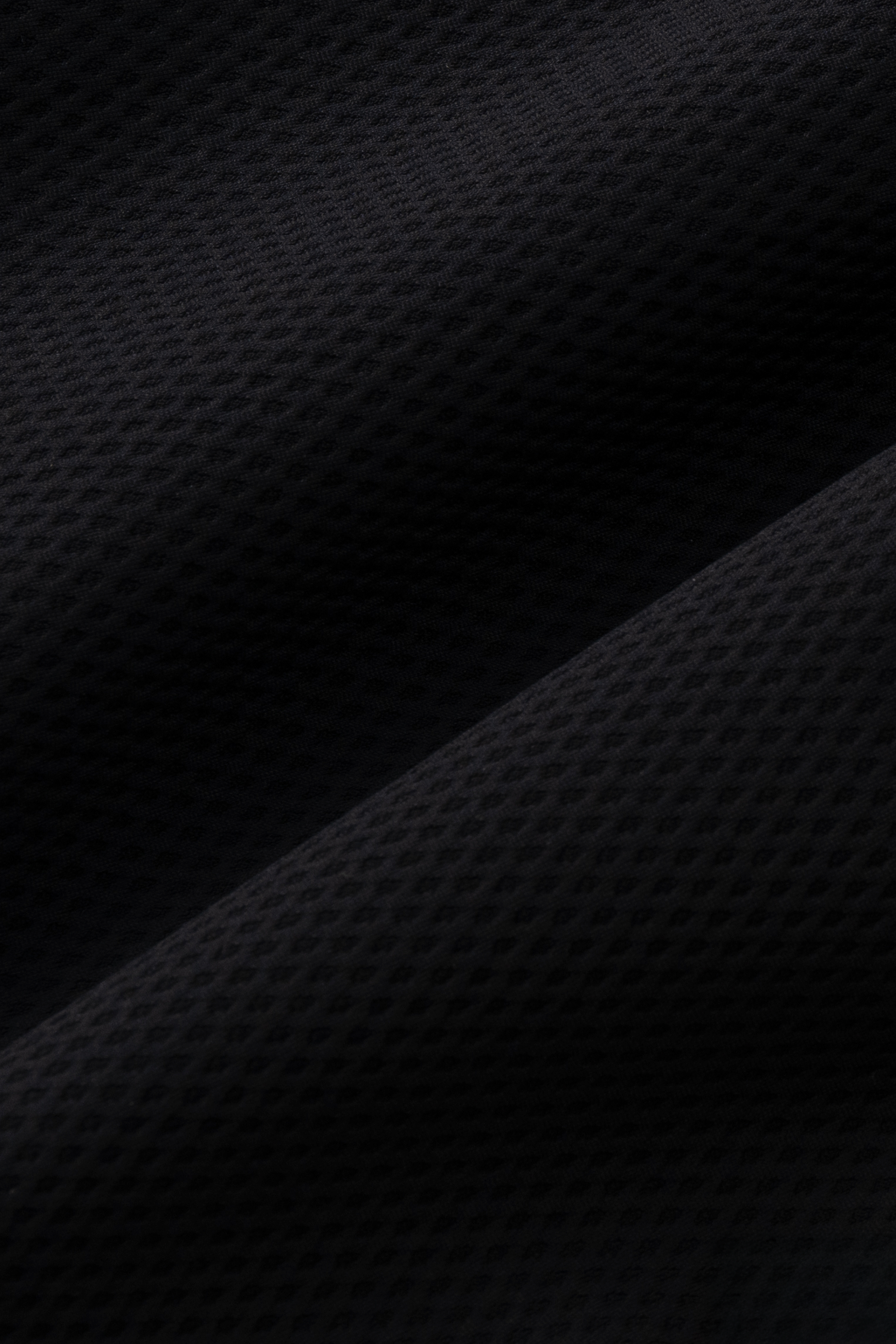 Close-up of Twillory's Air Quarter Zip in black, showcasing soft, wrinkle-free AIR fabric with a subtle geometric pattern, small dimples, and diagonal folds that highlight its comfortable stretch.