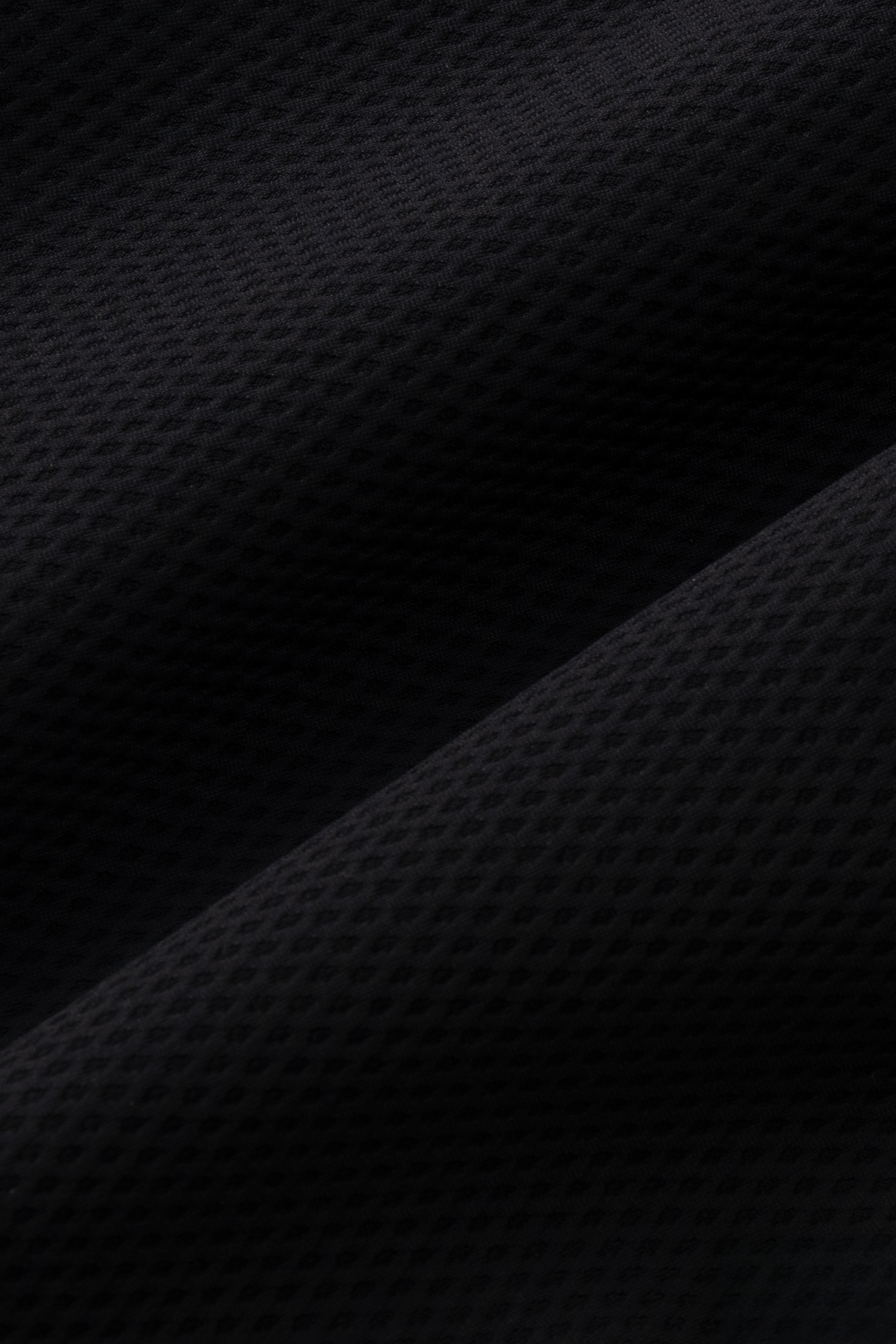 Close-up of Twillory's Air Quarter Zip in black, showcasing soft, wrinkle-free AIR fabric with a subtle geometric pattern, small dimples, and diagonal folds that highlight its comfortable stretch.