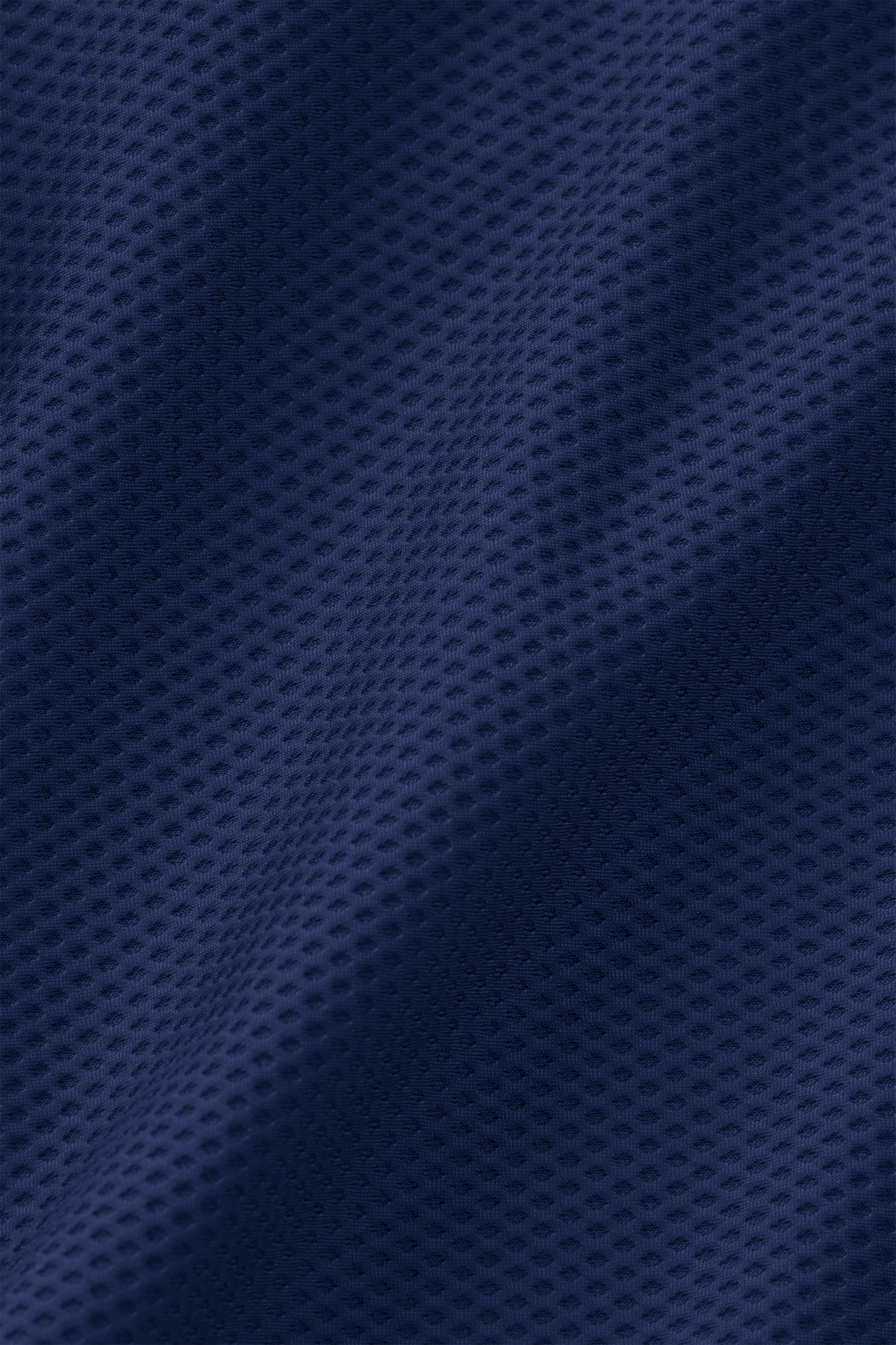 A close-up of the dark blue, textured AIR fabric from the Twillory Air Quarter Zip shows a small dimpled pattern with subtle folds and shadows, highlighting its soft, wrinkle-free stretch mesh.