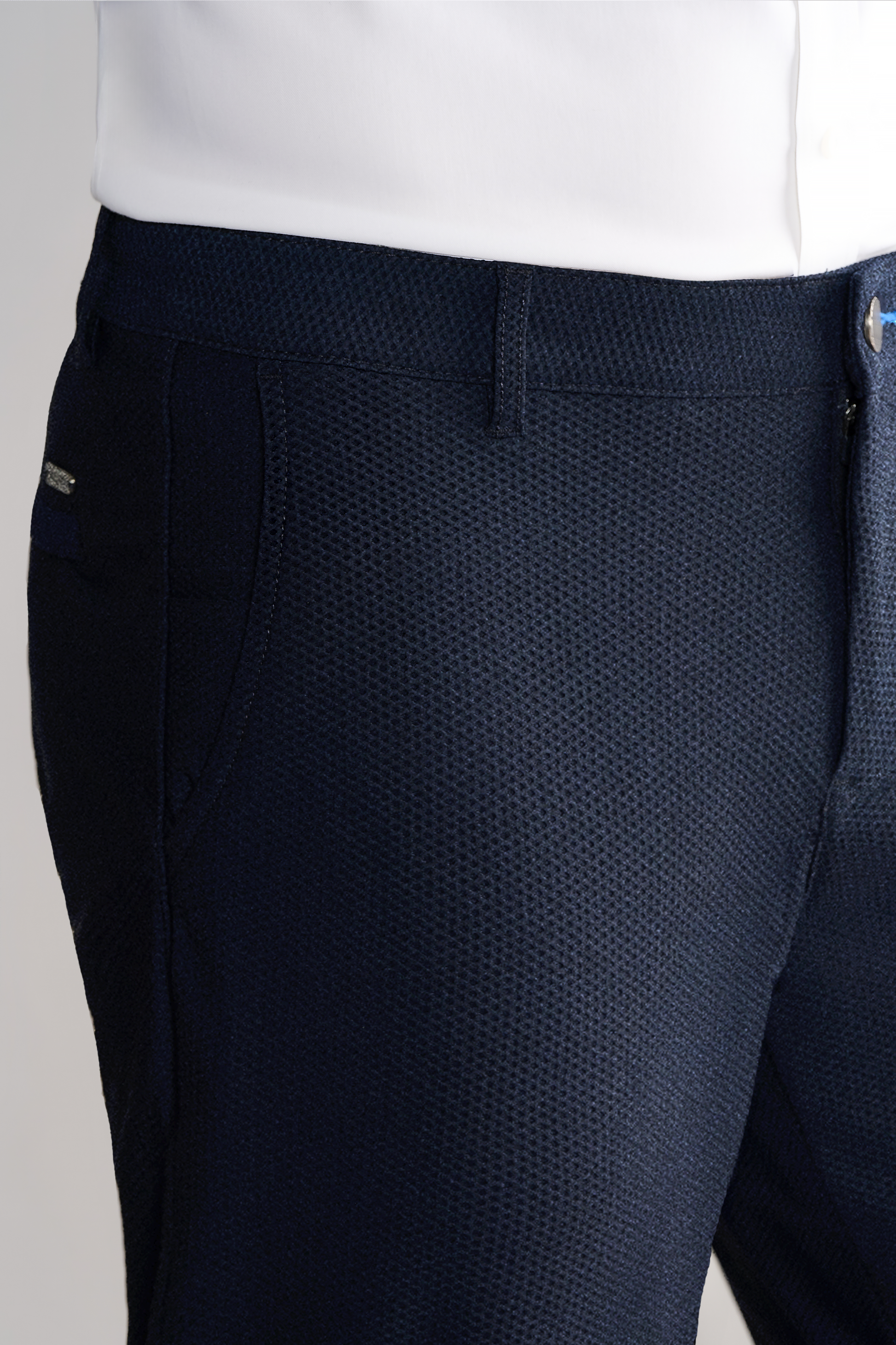Close-up of a person wearing Twillory AIR Pants // Heather Navy, crafted from 360° Airflow Fabric with a subtle woven texture, side pocket, belt loop, visible waistband with metallic tag detail. White shirt is tucked in.