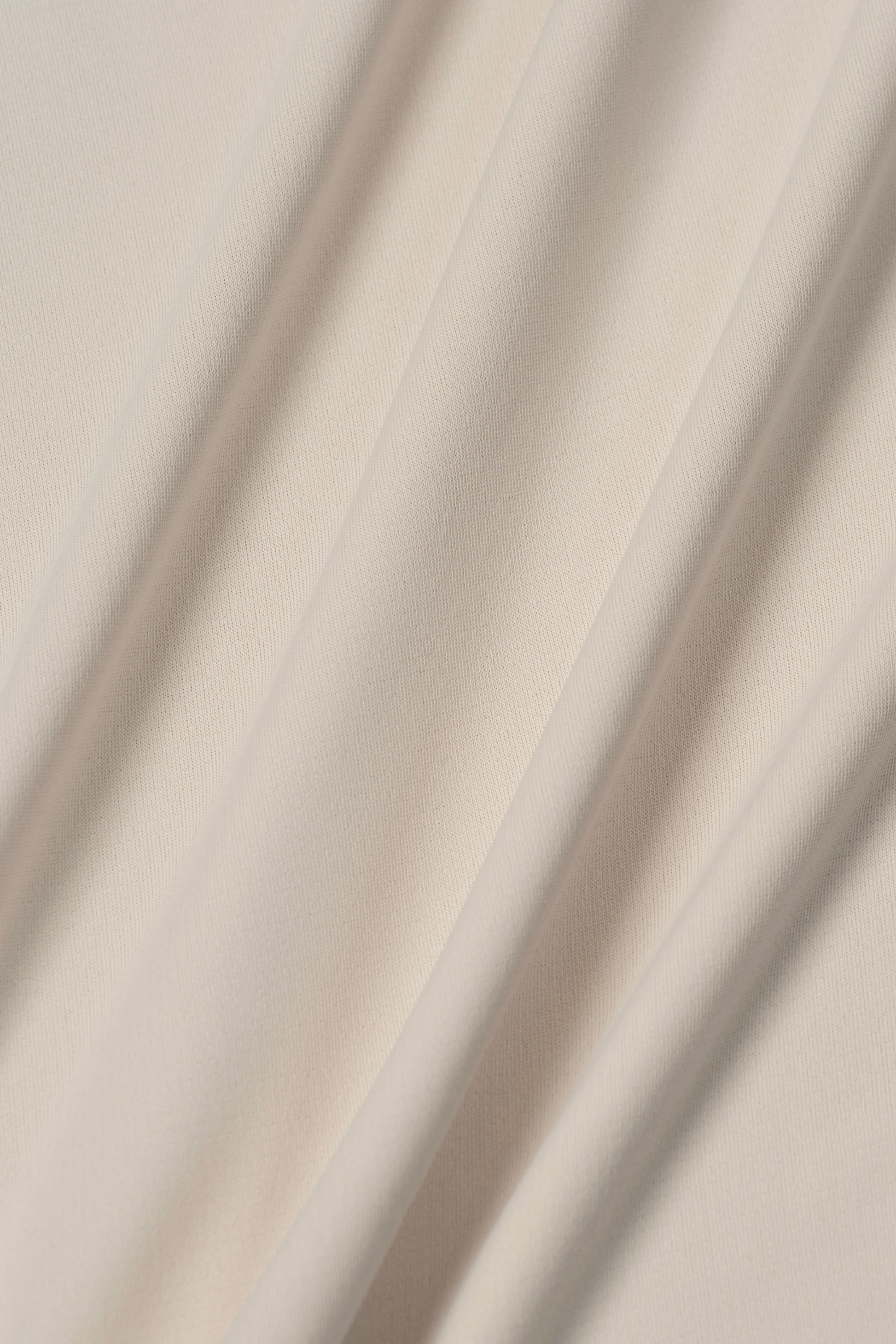 A close-up of the Long Sleeve Button Down Polo Solid in Ivory by Twillory shows soft, cream-colored fabric with diagonal folds and subtle shadows—its smooth, slightly stretchy material is ideal for a moisture-wicking performance polo shirt.
