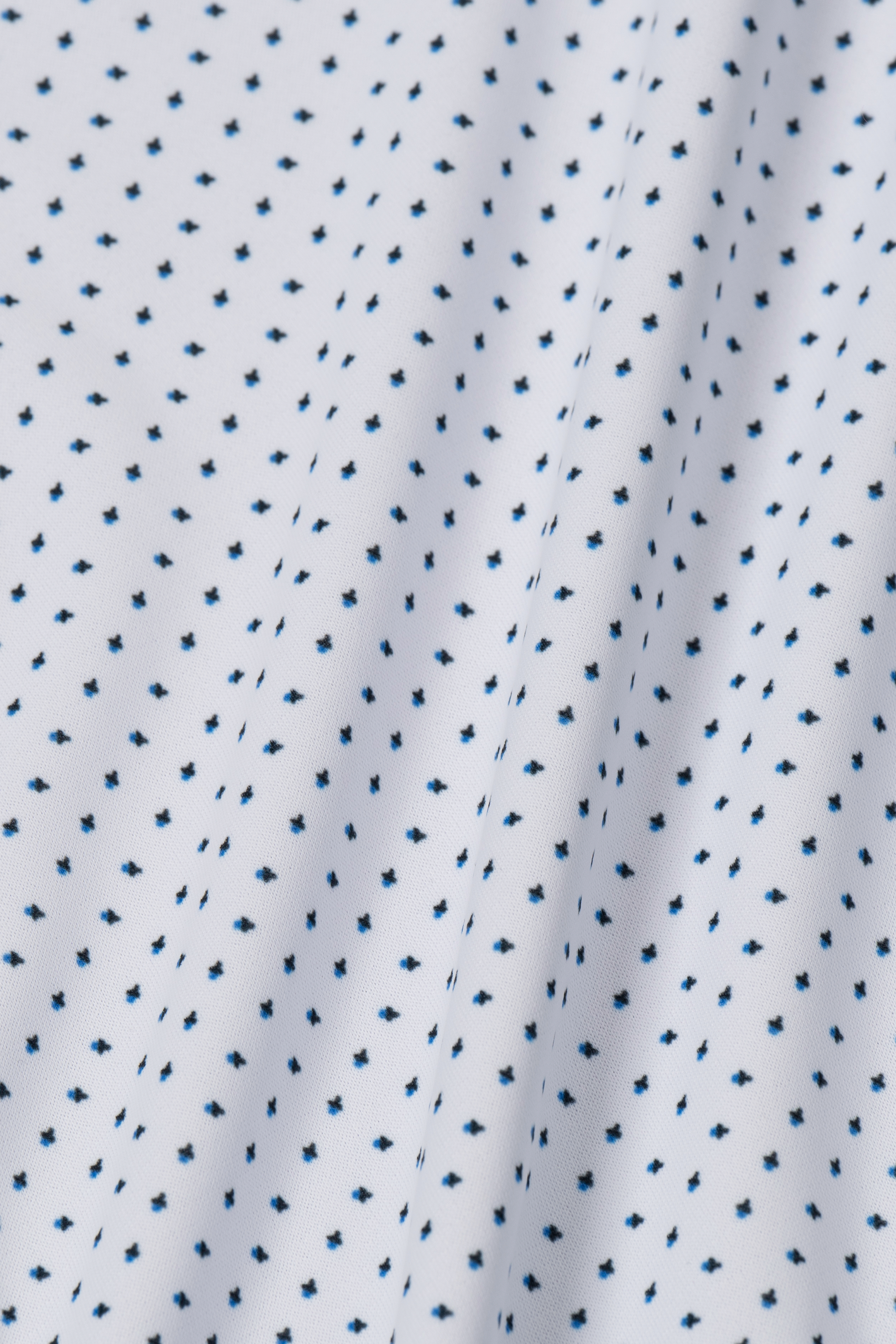 A close-up of Twillory’s Long Sleeve Button Down Polo Dot // Blue Acorn shows white moisture-wicking fabric with diagonal rows of small navy dots and gentle folds, adding texture—perfect for stylish, comfortable wear.