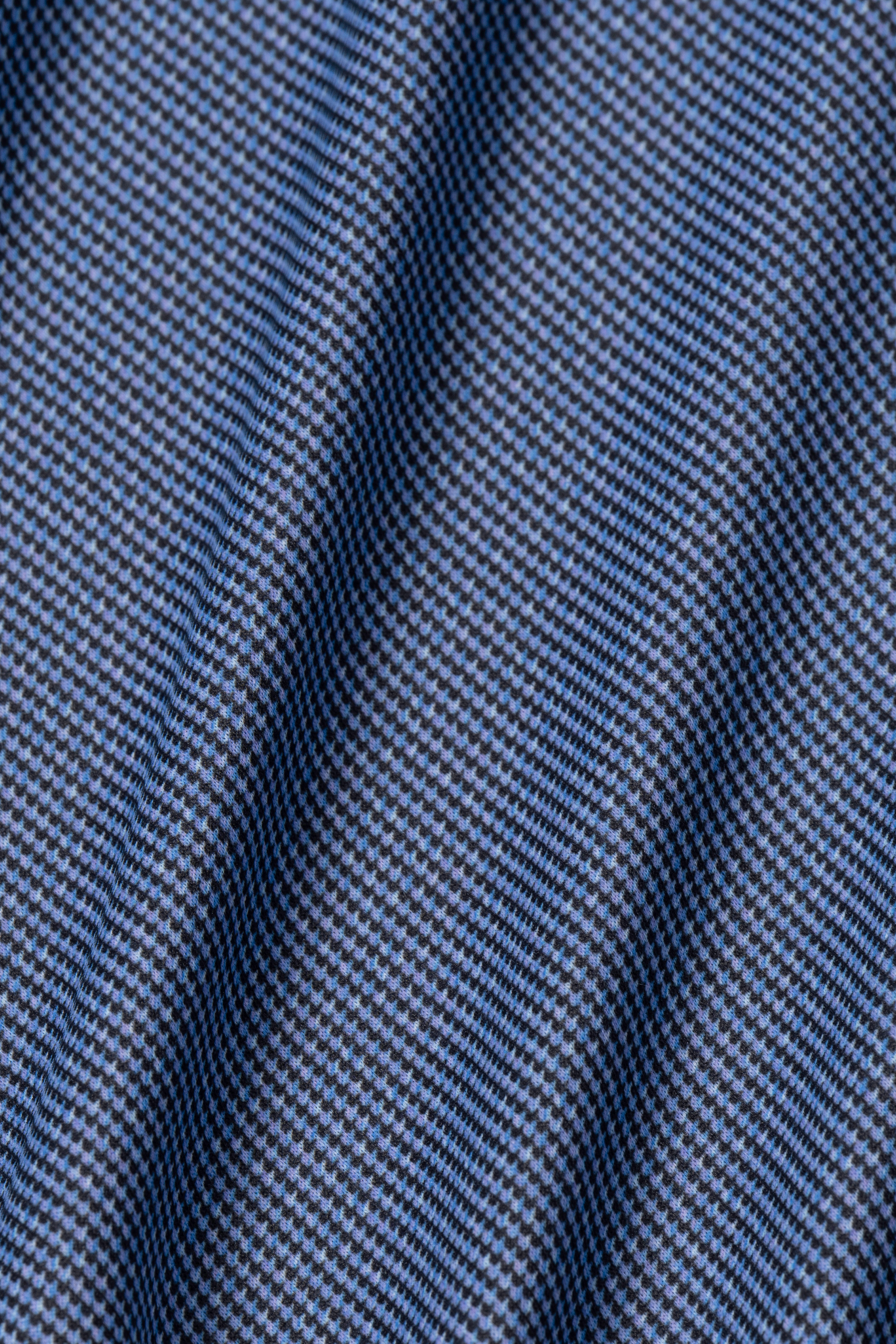 Close-up of the blue and black “Blue Puppytooth” fabric from Twillory’s Long Sleeve Button Down Polo Dot. The subtle geometric weave and sheen highlight the performance material, known for comfort and style.