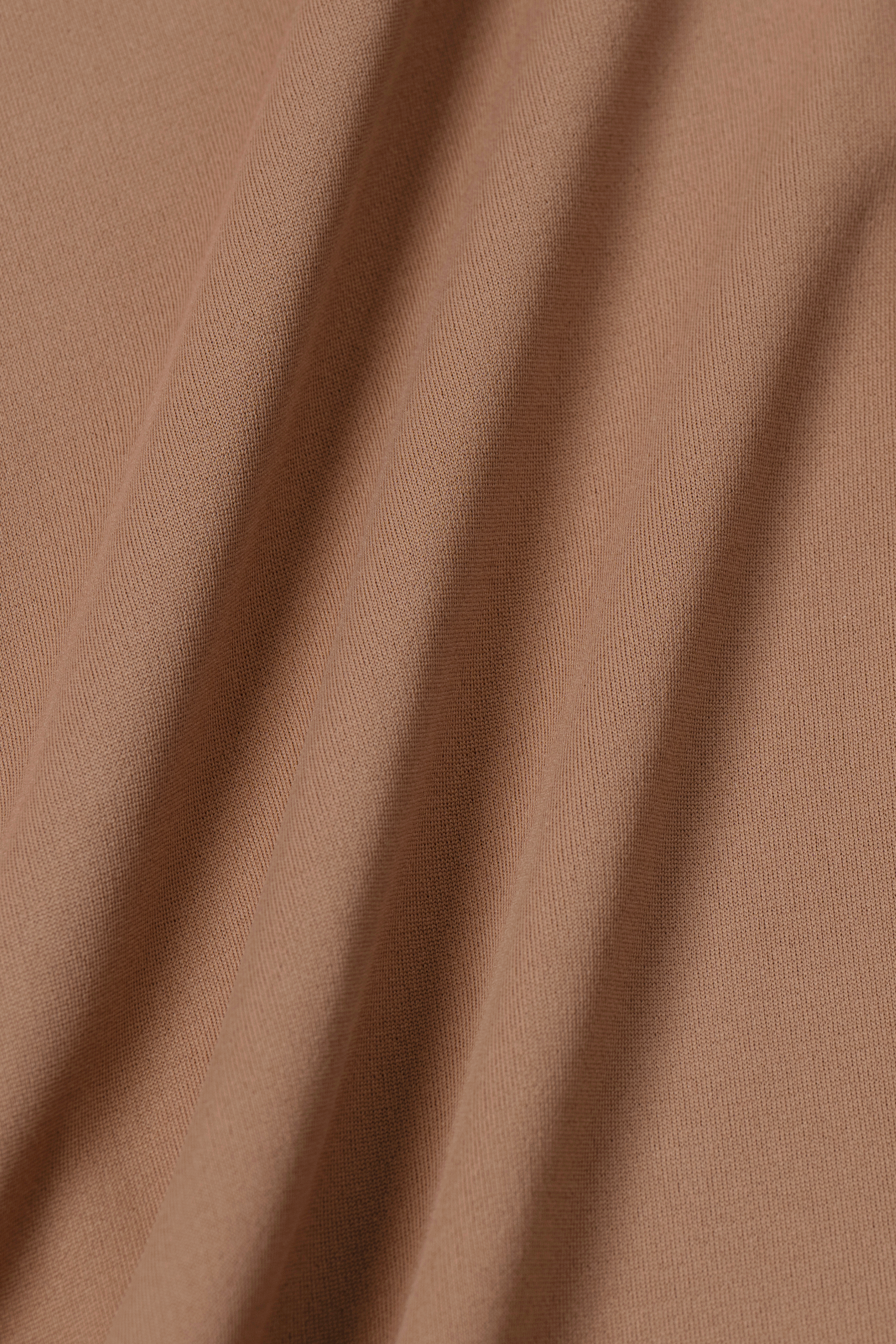 Close-up of tan, moisture-wicking fabric with a soft, smooth texture and gentle vertical folds, as featured in Twillory's Long Sleeve Button Down Polo Solid // Clay—designed for comfort and style in performance wear.