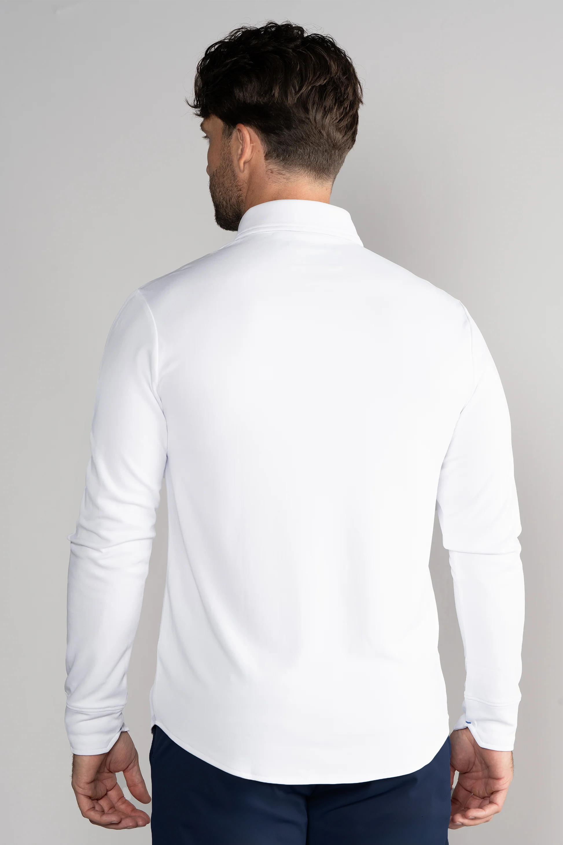 A man with short, dark, wavy hair is seen from behind wearing the Twillory Long Sleeve Button Down Polo Contrast in White Navy, standing against a light gray background with his arms relaxed at his sides.