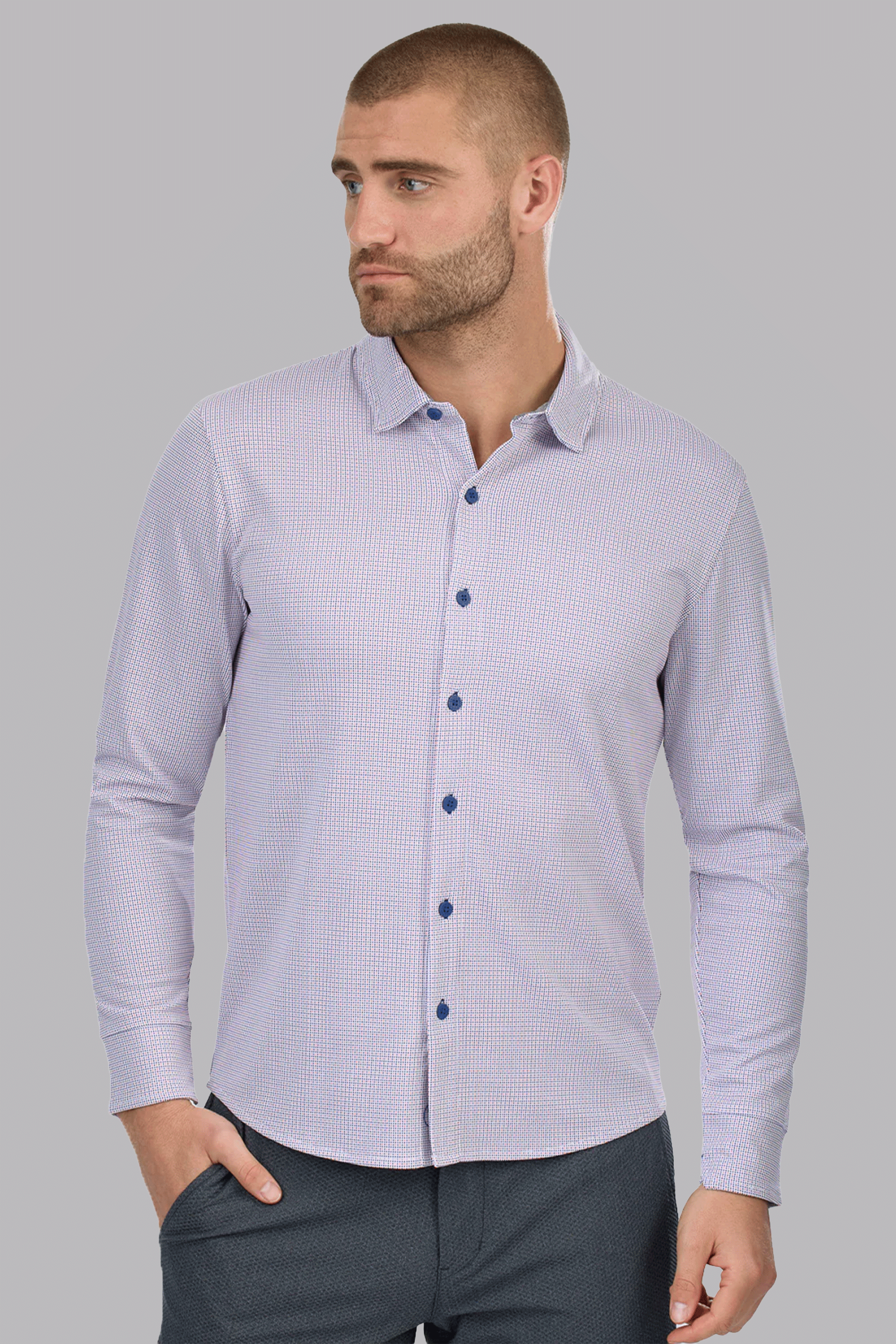 A man with closely-cropped hair and a beard wears the Twillory Long Sleeve Button Down Polo Dot in Orange Blue, featuring blue buttons and a subtle dotted pattern. He looks to his left with one hand in his pocket against a light gray background.