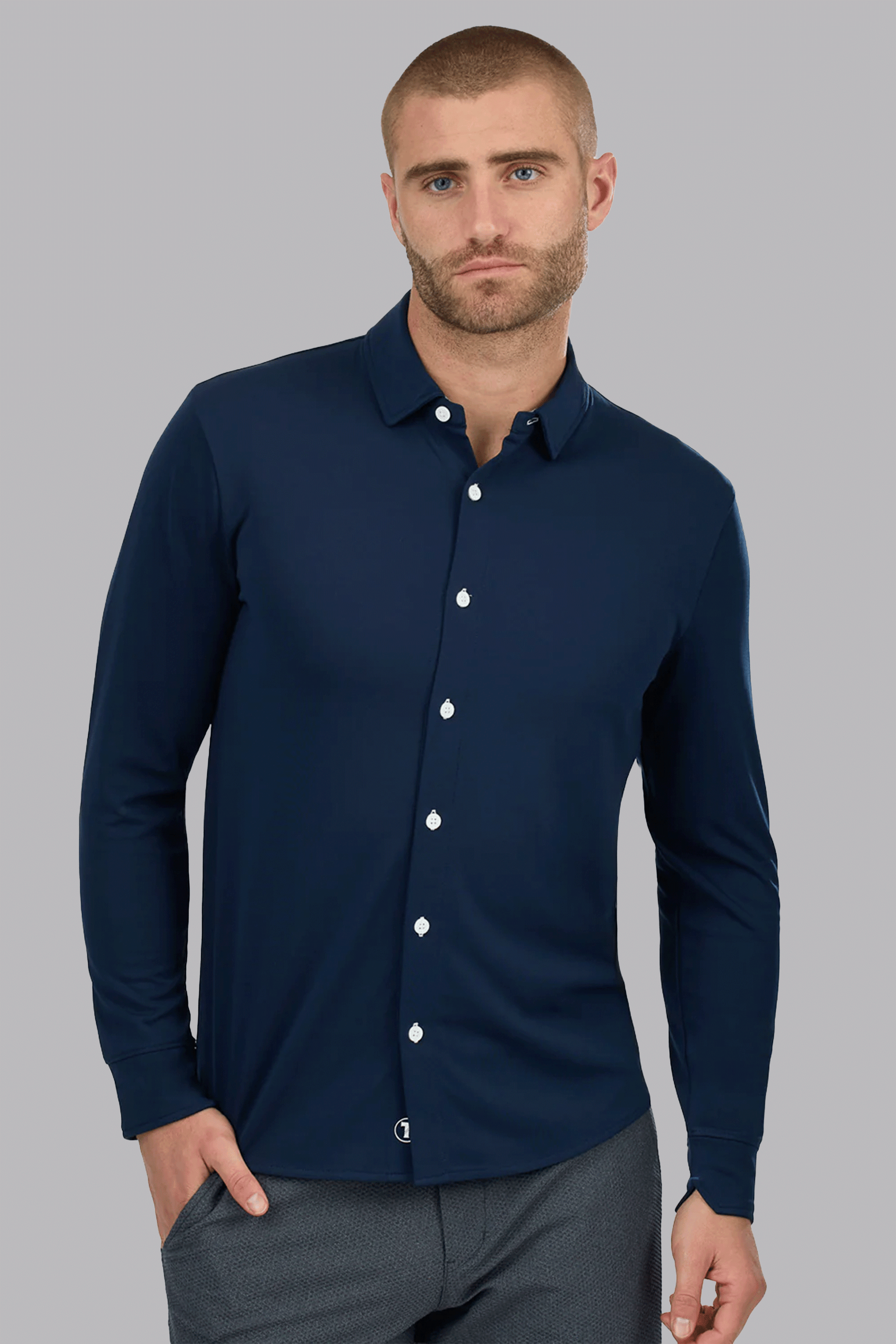A man with closely cropped hair and a beard wears the Twillory Long Sleeve Button Down Polo Contrast in Navy White. One hand is in his pocket as he stands against a plain light gray background, looking directly at the camera with a neutral expression.
