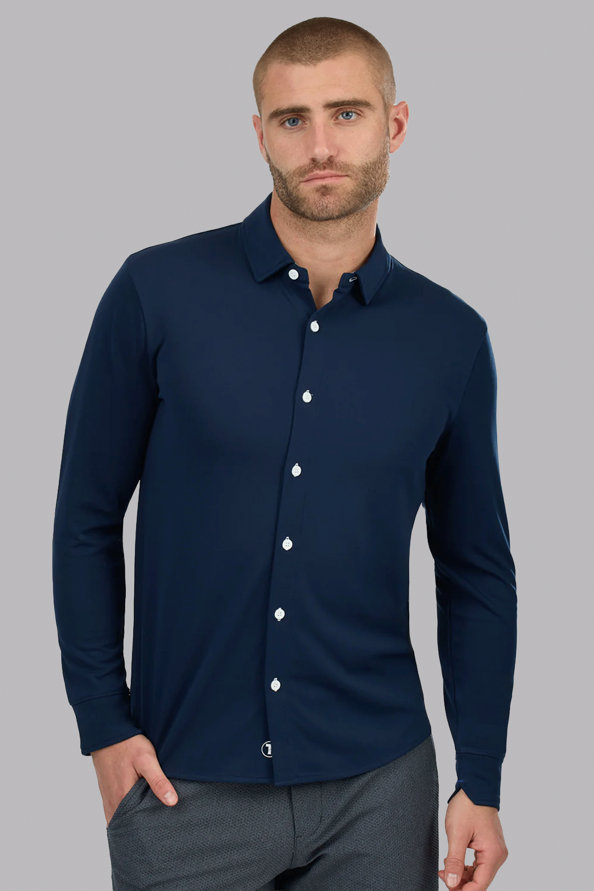 A man with closely cropped hair and a beard wears the Twillory Long Sleeve Button Down Polo Contrast in Navy White. One hand is in his pocket as he stands against a plain light gray background, looking directly at the camera with a neutral expression.