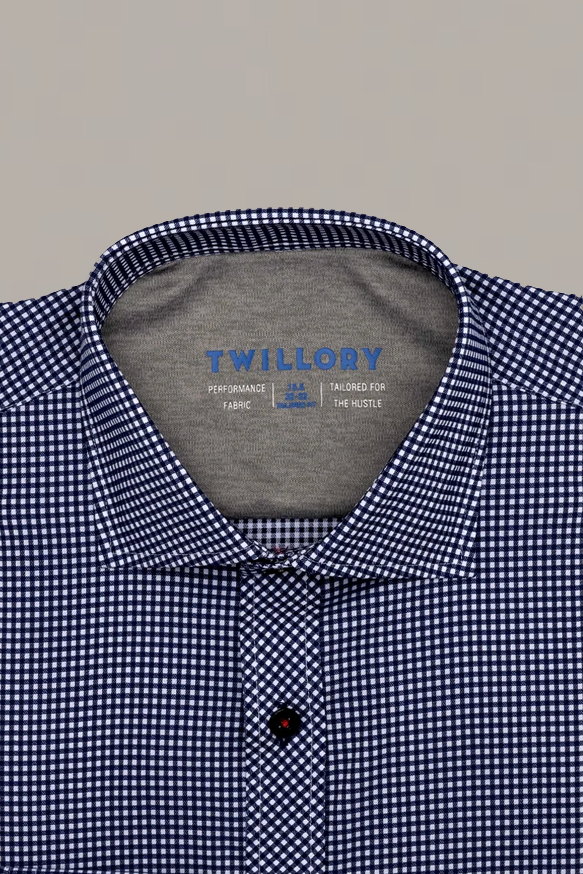 A close-up of the Twillory Leader Check // Blue shirt, neatly folded. The inside collar features "TWILLORY" and "TAILORED FOR THE HUSTLE" in blue text. This 4-way stretch gingham shirt rests on a plain light gray background.