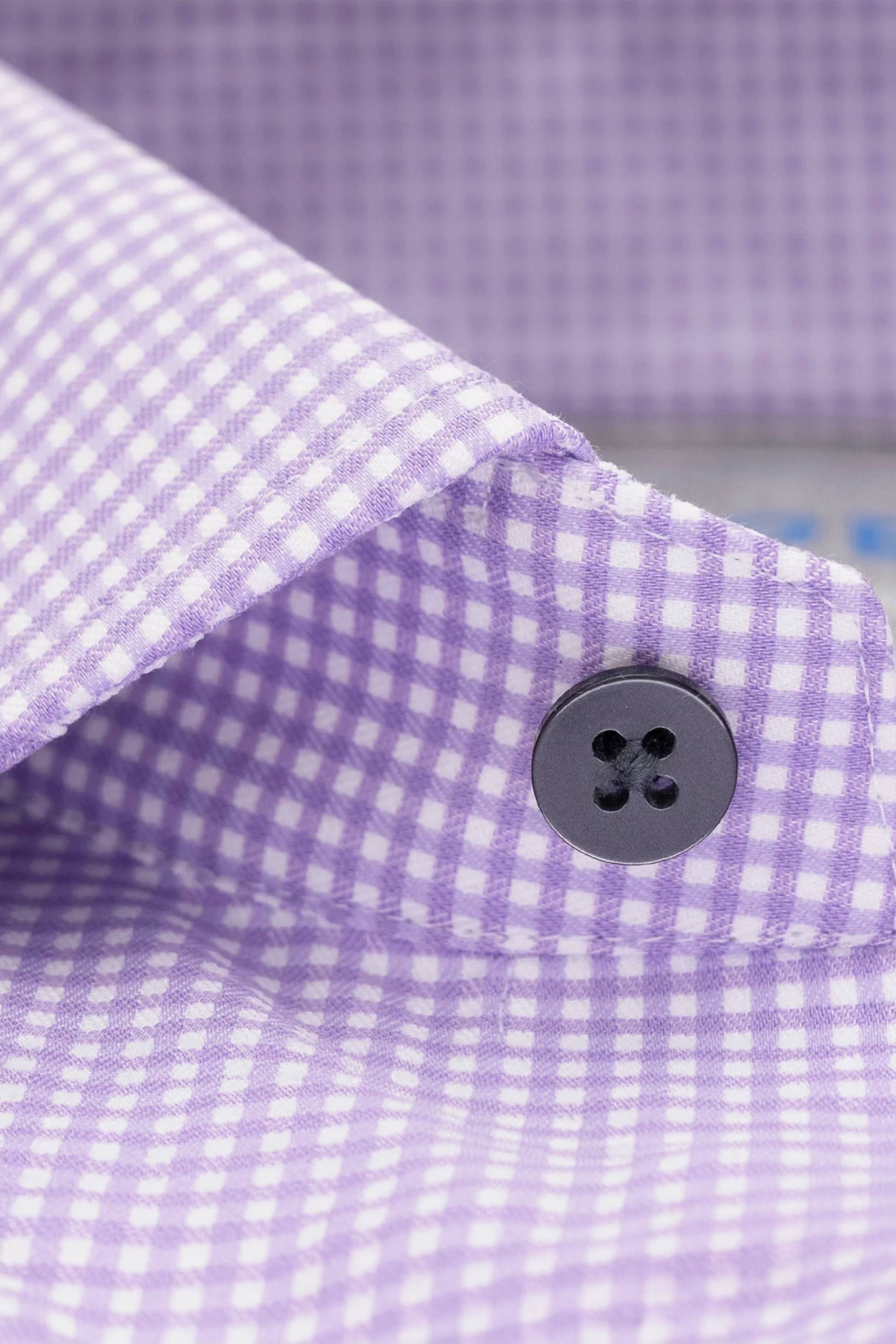 Close-up of the Twillory Leader Check // Lavender shirt collar, showcasing its lavender and white checks with a black four-hole button. The crisp fabric and precise pattern offer a classic, comfortable look for all-day wear.