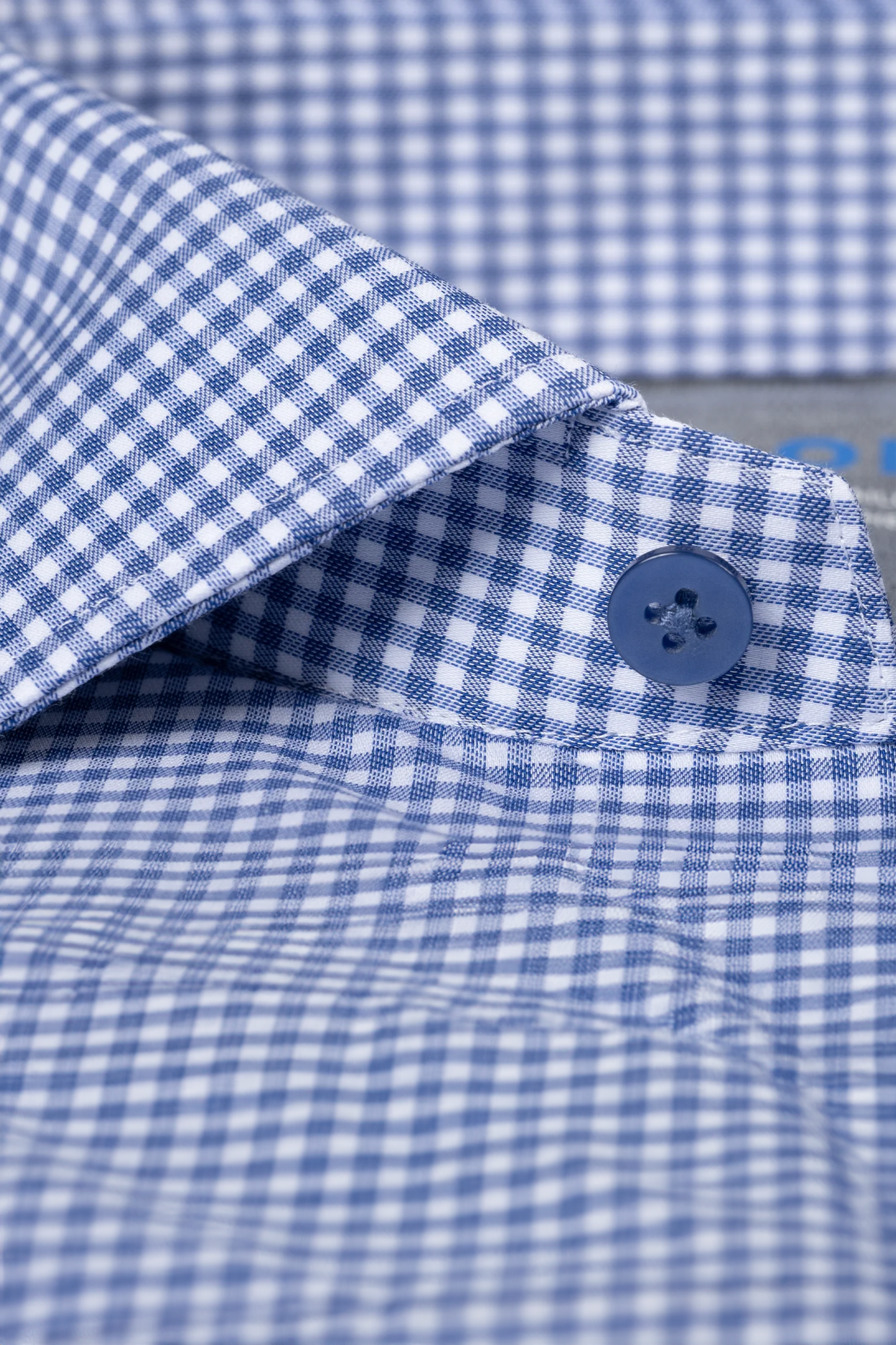 Close-up of Twillory’s Leader Check // Micro Blue shirt, displaying blue and white gingham fabric with 4-way stretch, a sharp collar, blue button, and neat stitching highlighting its crisp construction.