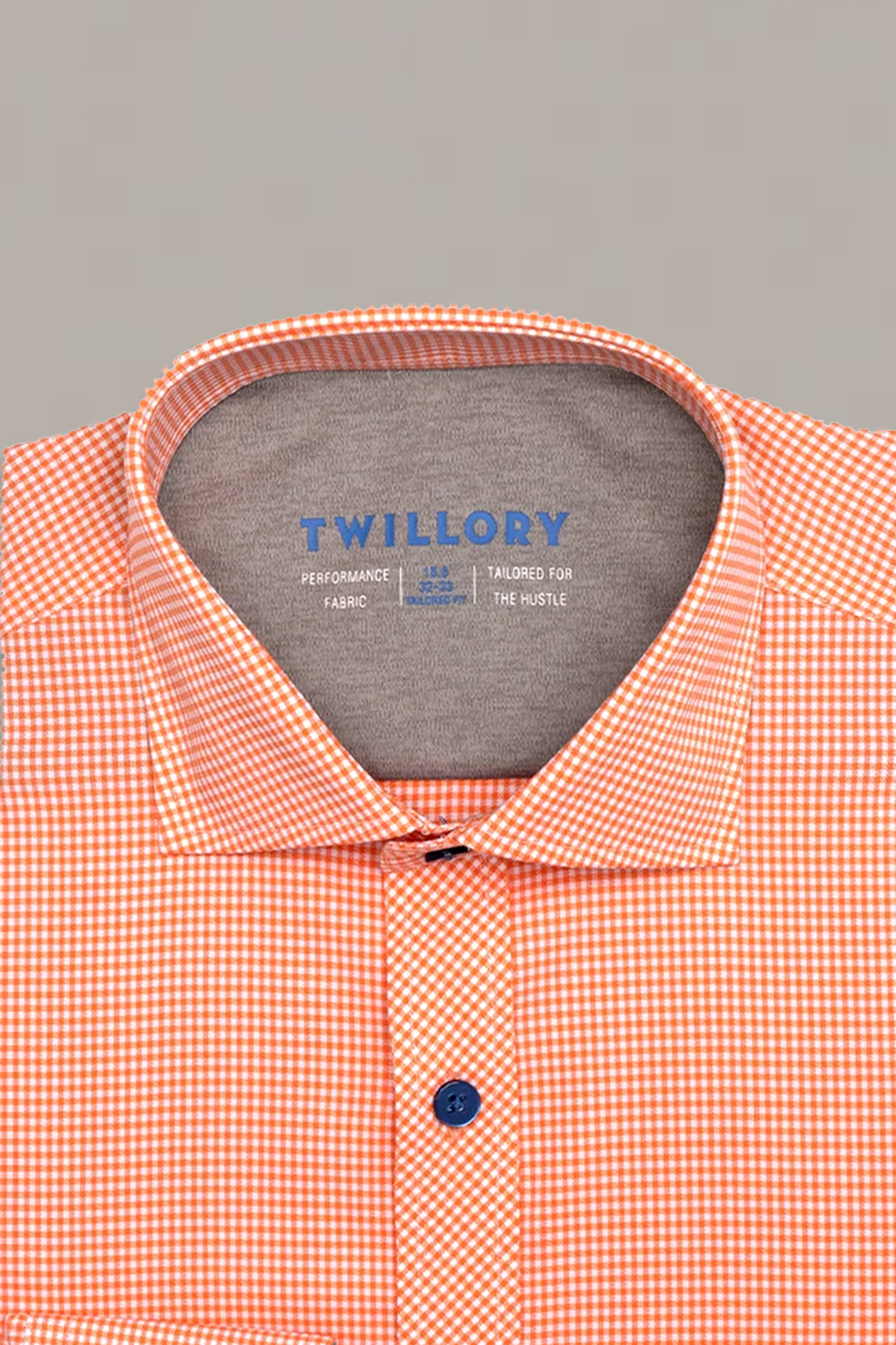 A neatly folded Twillory Leader Check // Orange shirt with a collar and blue buttons, featuring a small orange and white check, 4-way stretch fabric, and a “Twillory PERFORMANCE FABRIC TAILORED FOR THE HUSTLE” label on a light background.
