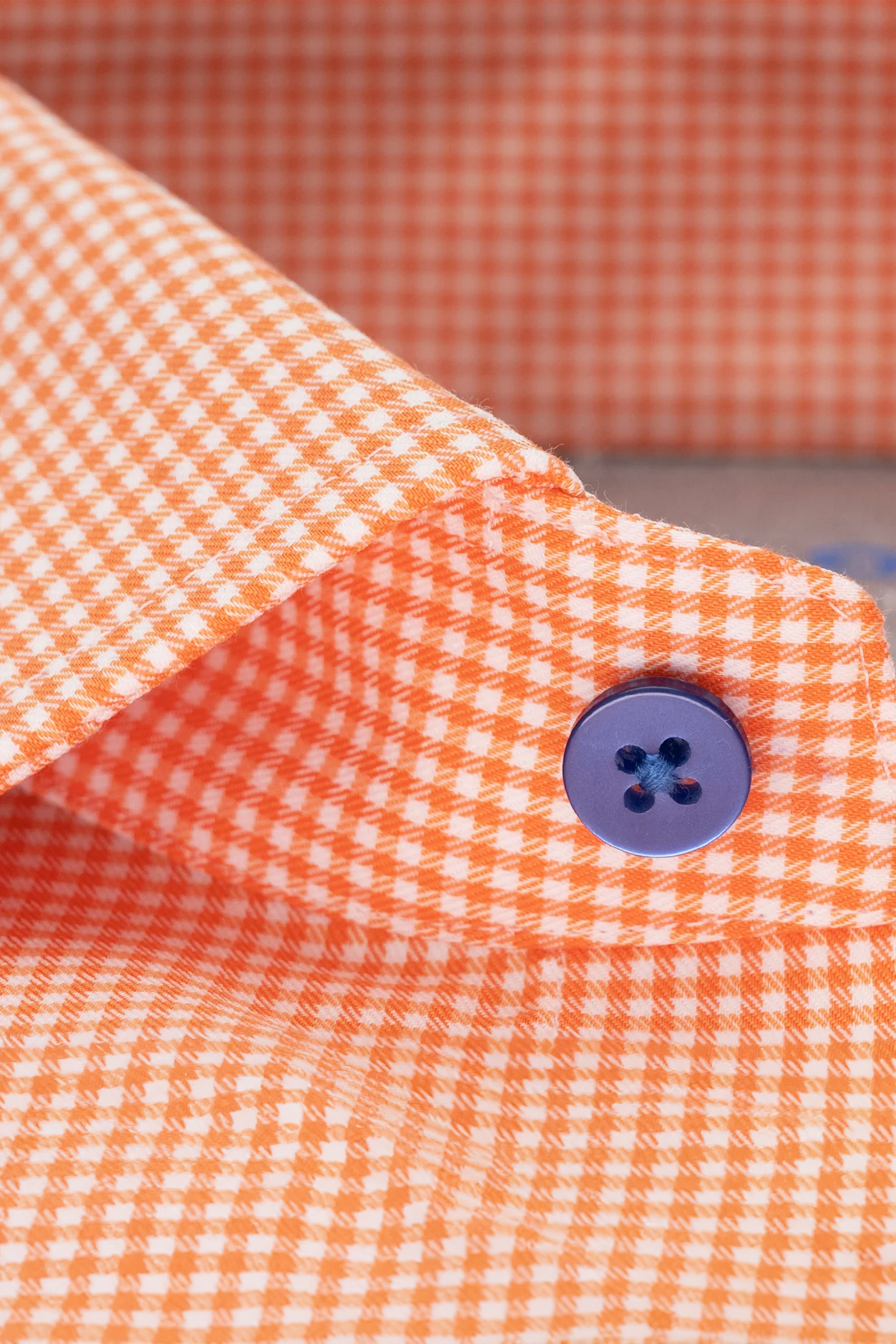 Close-up of the Twillory Leader Check // Orange shirt collar, featuring orange and white gingham fabric, a blue four-hole button, detailed stitching, crisp folds, and moisture-wicking material.