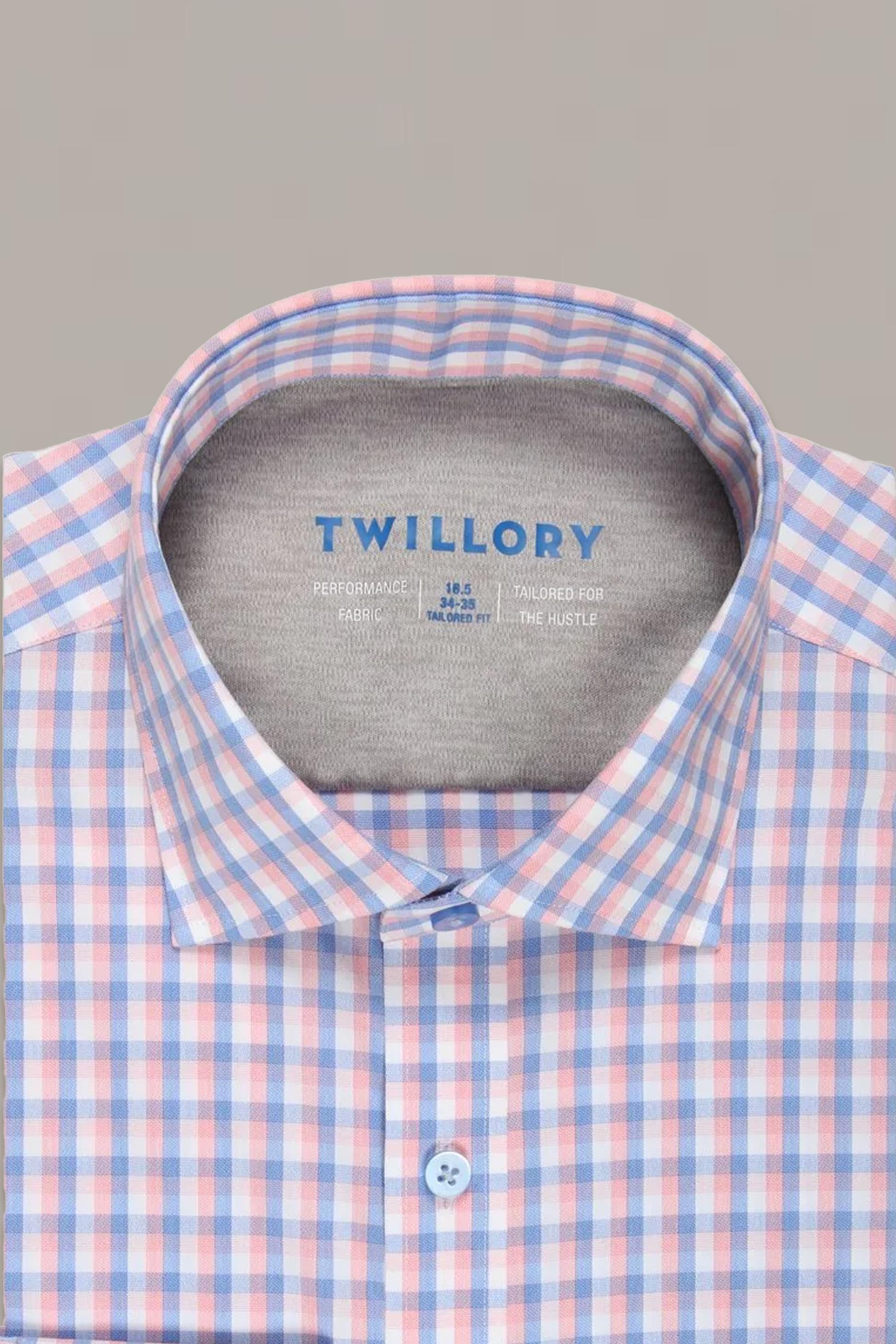 A neatly folded, buttoned-down Twillory Leader Check // Orange Blue dress shirt with an orange and blue check pattern. Features 4-way stretch for comfort. "TWILLORY" is printed in blue inside the gray collar. Plain light beige background.
