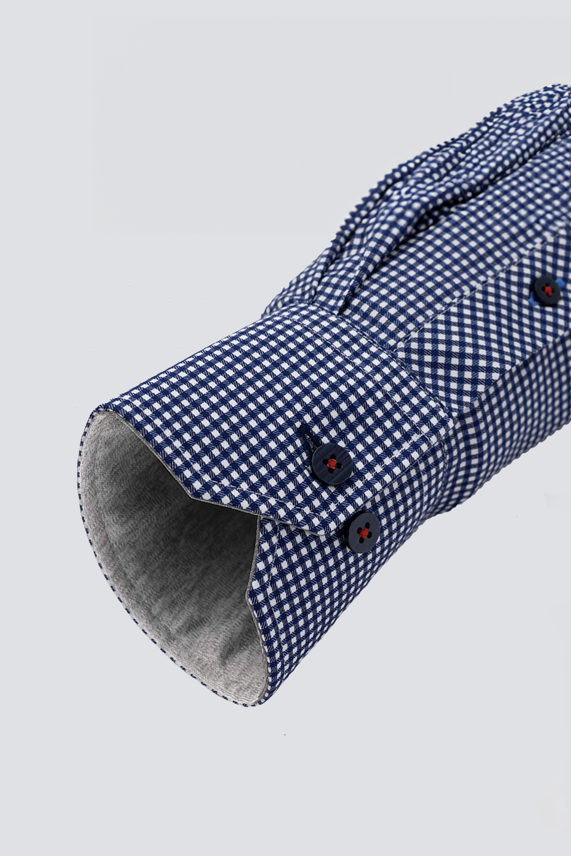 A close-up of Twillory’s Leader Check // Blue shirt cuff, showing blue and white checkered fabric, navy buttons with red thread, soft gray lining, neat stitching, and moisture-wicking comfort. The shirt is laid flat on a light gray background.