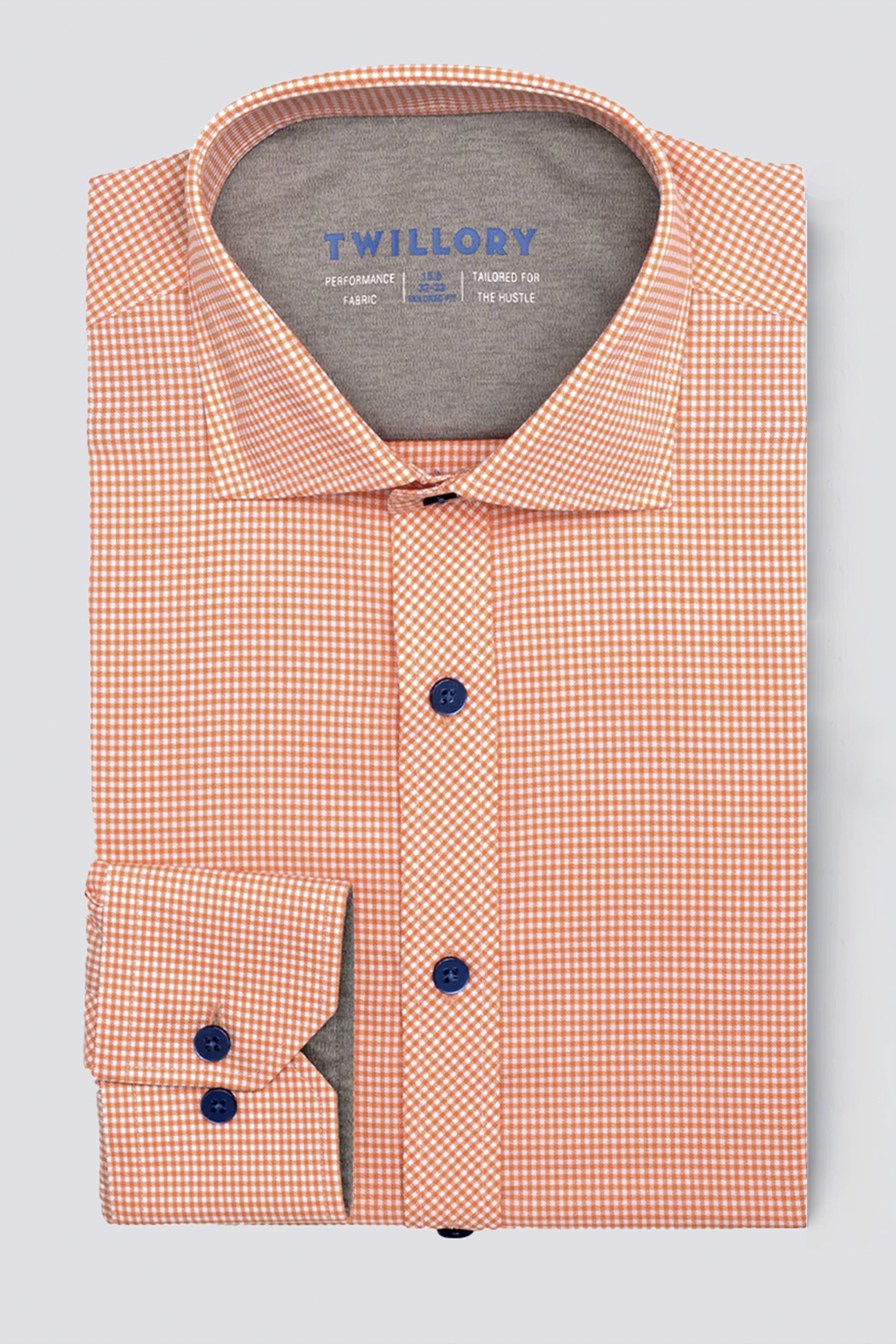 The Twillory Leader Check // Orange shirt features a neatly folded orange and white checkered pattern, blue buttons, wide collar, and visible Twillory label. This 4-way stretch dress shirt is displayed on a light gray background.