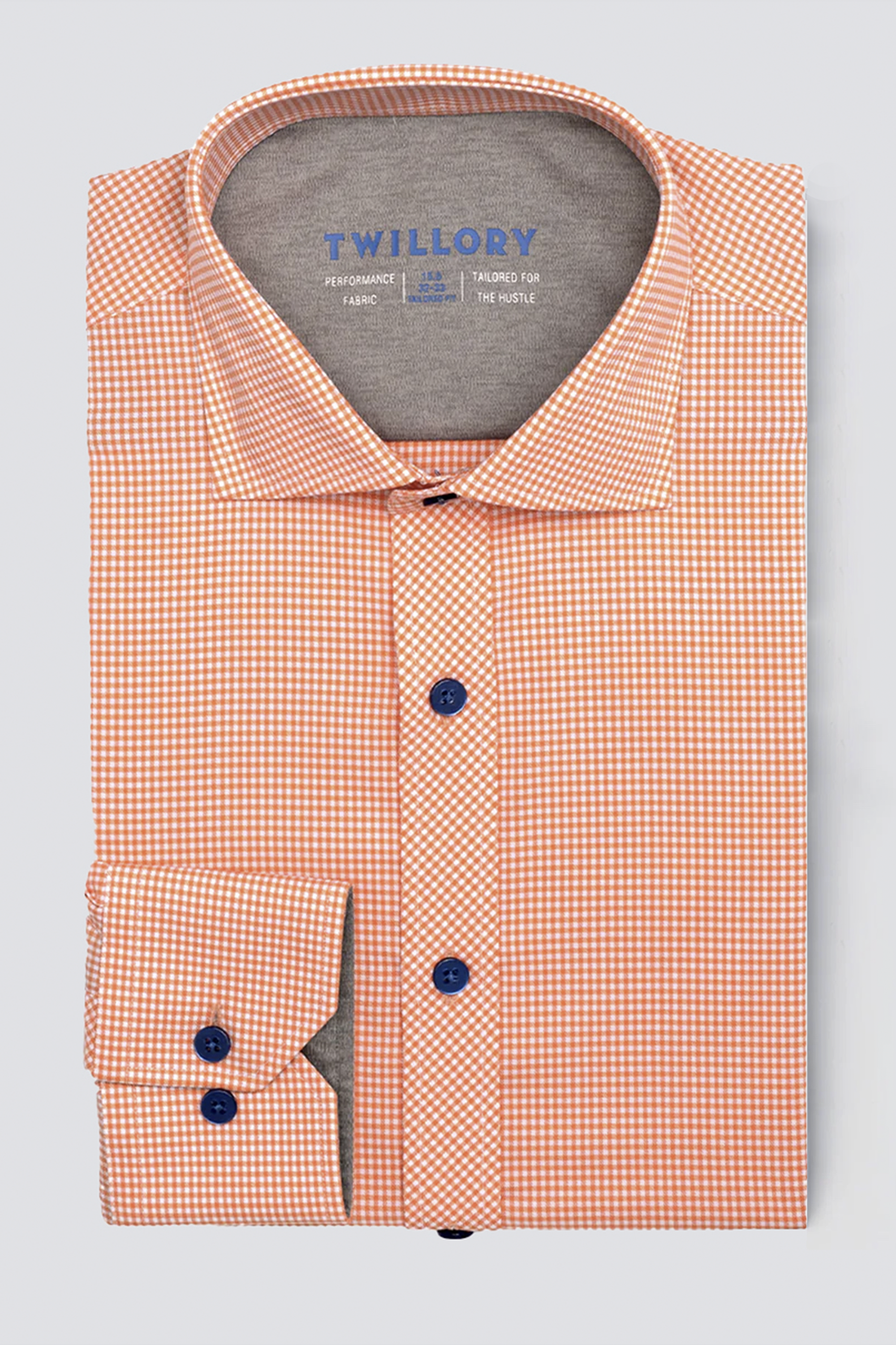 The Twillory Leader Check // Orange shirt features a neatly folded orange and white checkered pattern, blue buttons, wide collar, and visible Twillory label. This 4-way stretch dress shirt is displayed on a light gray background.