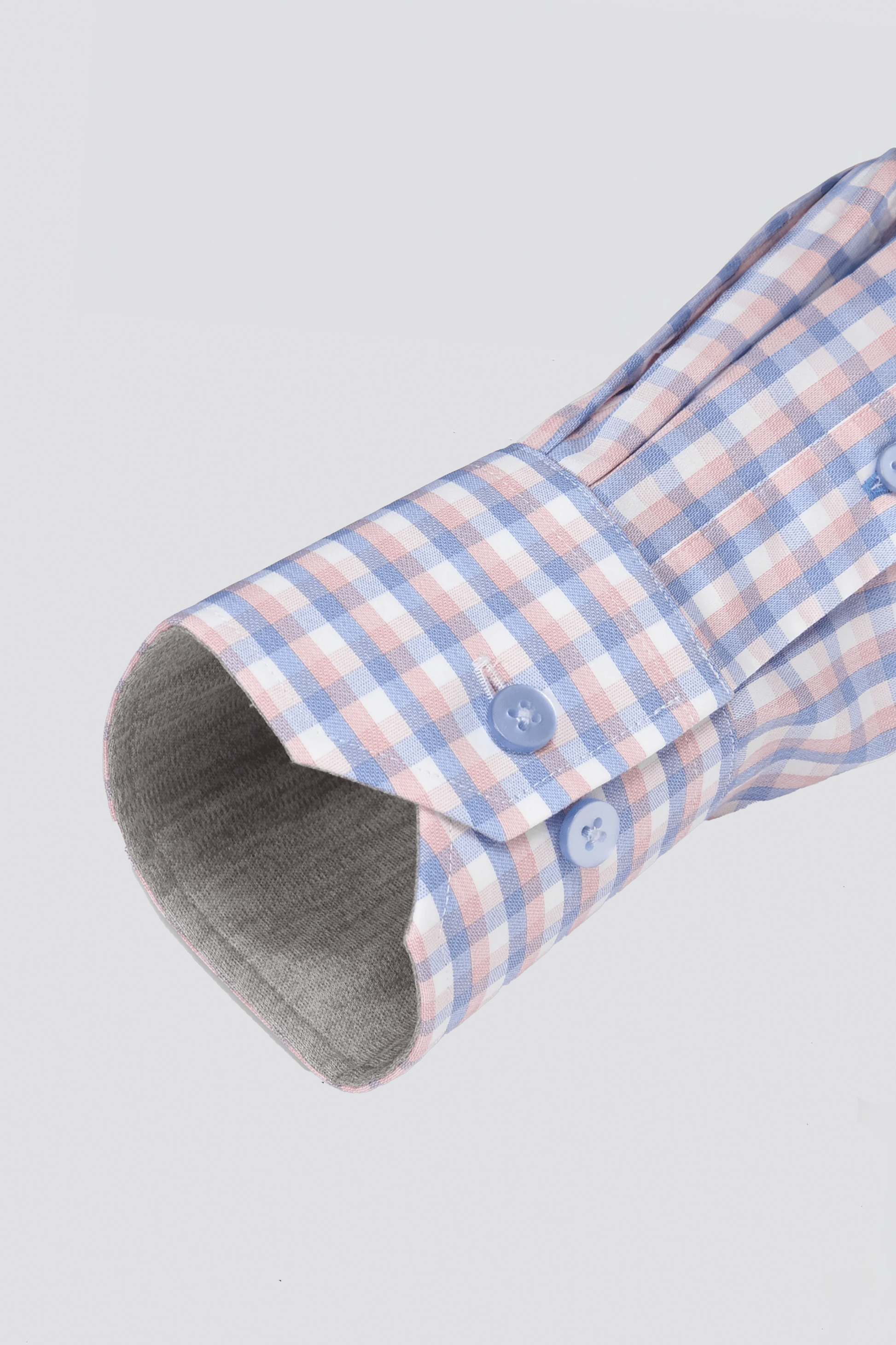 A close-up of the Twillory Leader Check // Orange Blue shirt sleeve, showcasing its 4-way stretch fabric in an orange and blue check pattern. The cuff, with two light blue buttons and soft grey lining, is set against a plain light grey background.