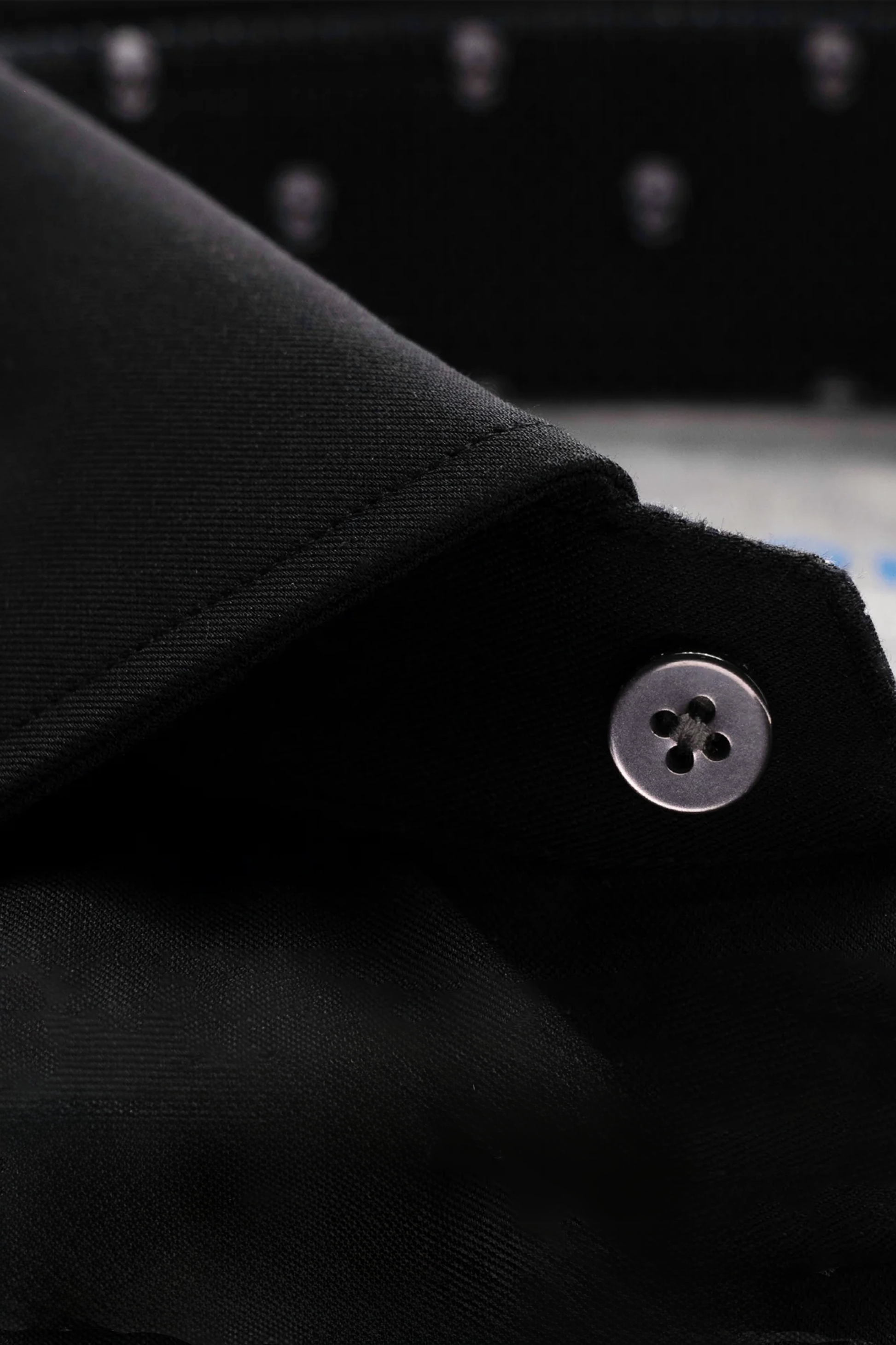 Close-up of Twillory's Leader Contrast // Black Skull shirt: a black performance top with a folded collar, silvery four-hole button, moisture-wicking matte fabric, and an inner collar featuring a subtle skull pattern on a dark background.