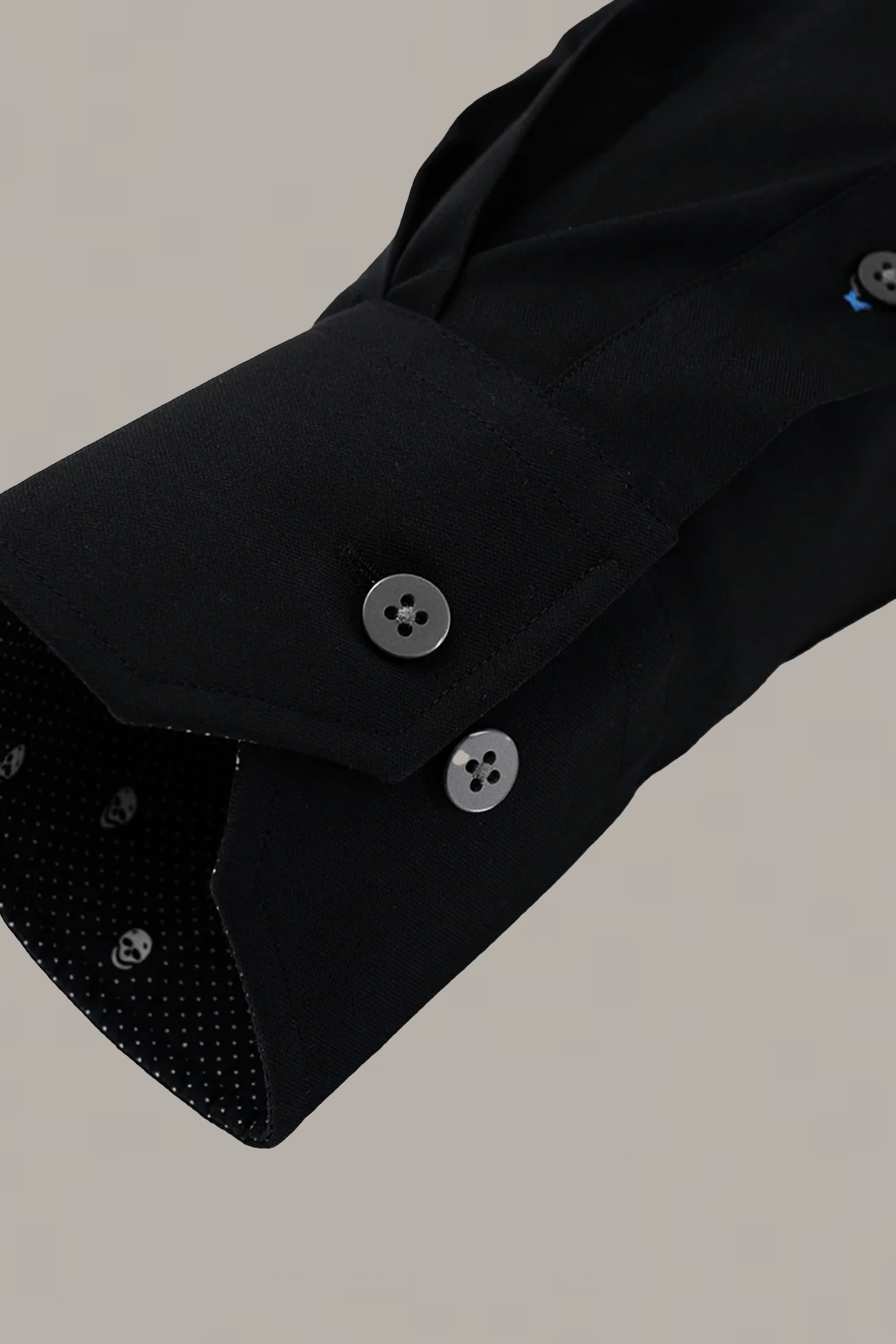 A close-up of the Leader Contrast // Black Skull by Twillory shows a black performance shirt sleeve with two black cuff buttons and an open cuff, revealing a subtly dotted black inner lining against a plain light grey background.