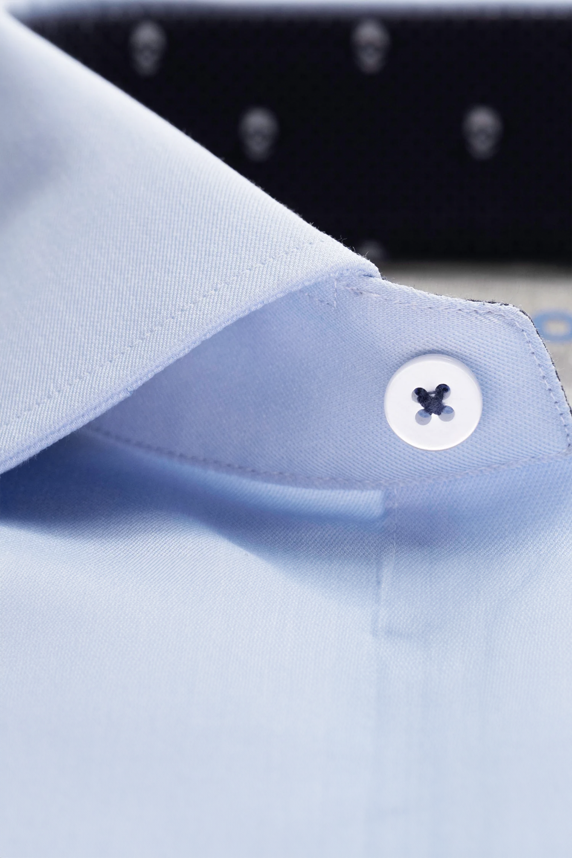 Close-up of the Twillory Leader Contrast // Blue Skull shirt collar with a white button. The light blue fabric features smooth, 4-way stretch material, while the inner lining reveals a dark pattern with subtle white polka dots inside the collar.