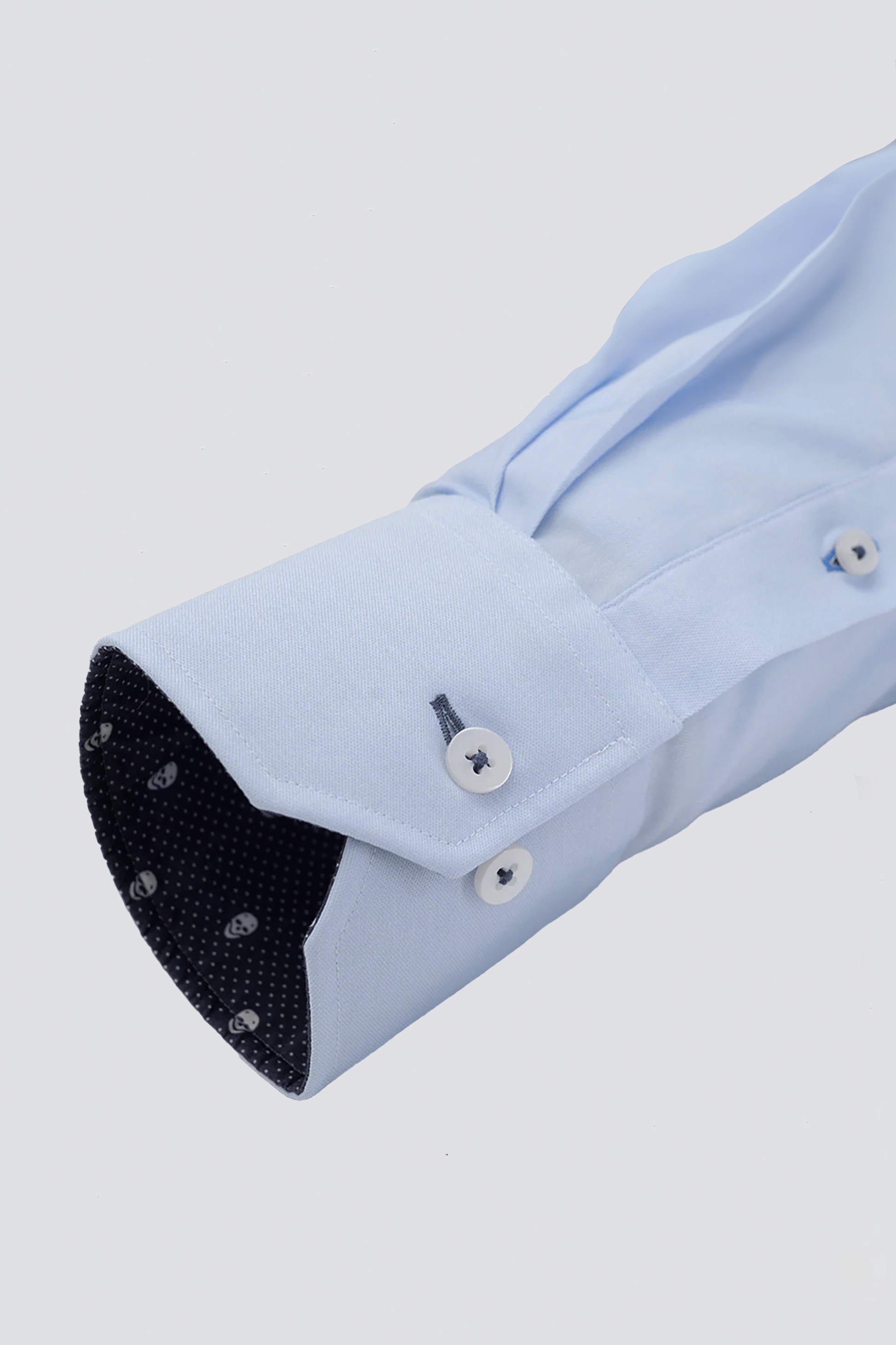 A close-up of Twillory’s Leader Contrast // Blue Skull Performance Shirt shows the light blue sleeve cuff with two white buttons, detailed stitching, and a dark inner lining featuring a subtle white skull pattern against a plain background.