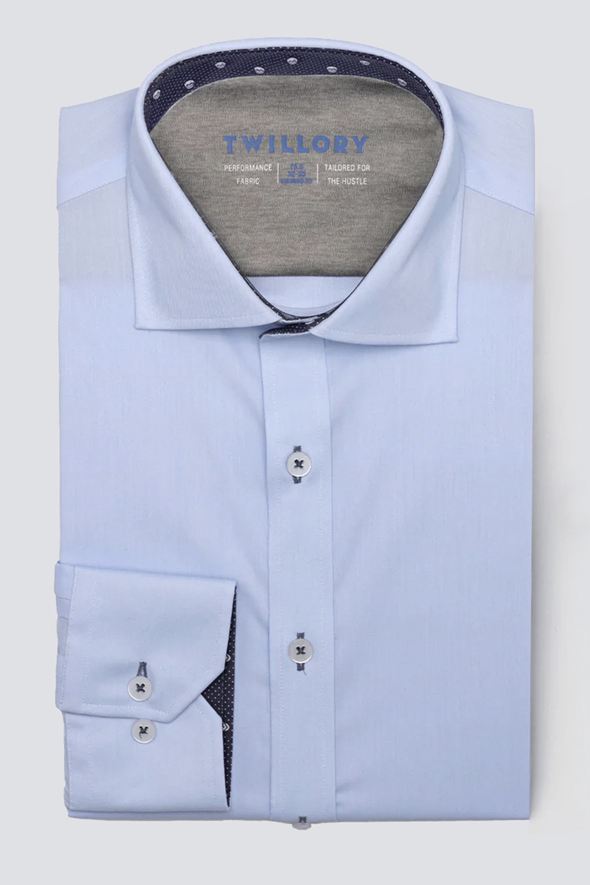 A neatly folded Twillory Leader Contrast // Blue Skull Performance Shirt in light blue with a spread collar, white buttons, dark blue threads, and navy polka dot lining inside the collar/cuffs. Features 4-way stretch and “Twillory” branding on the inner collar.
