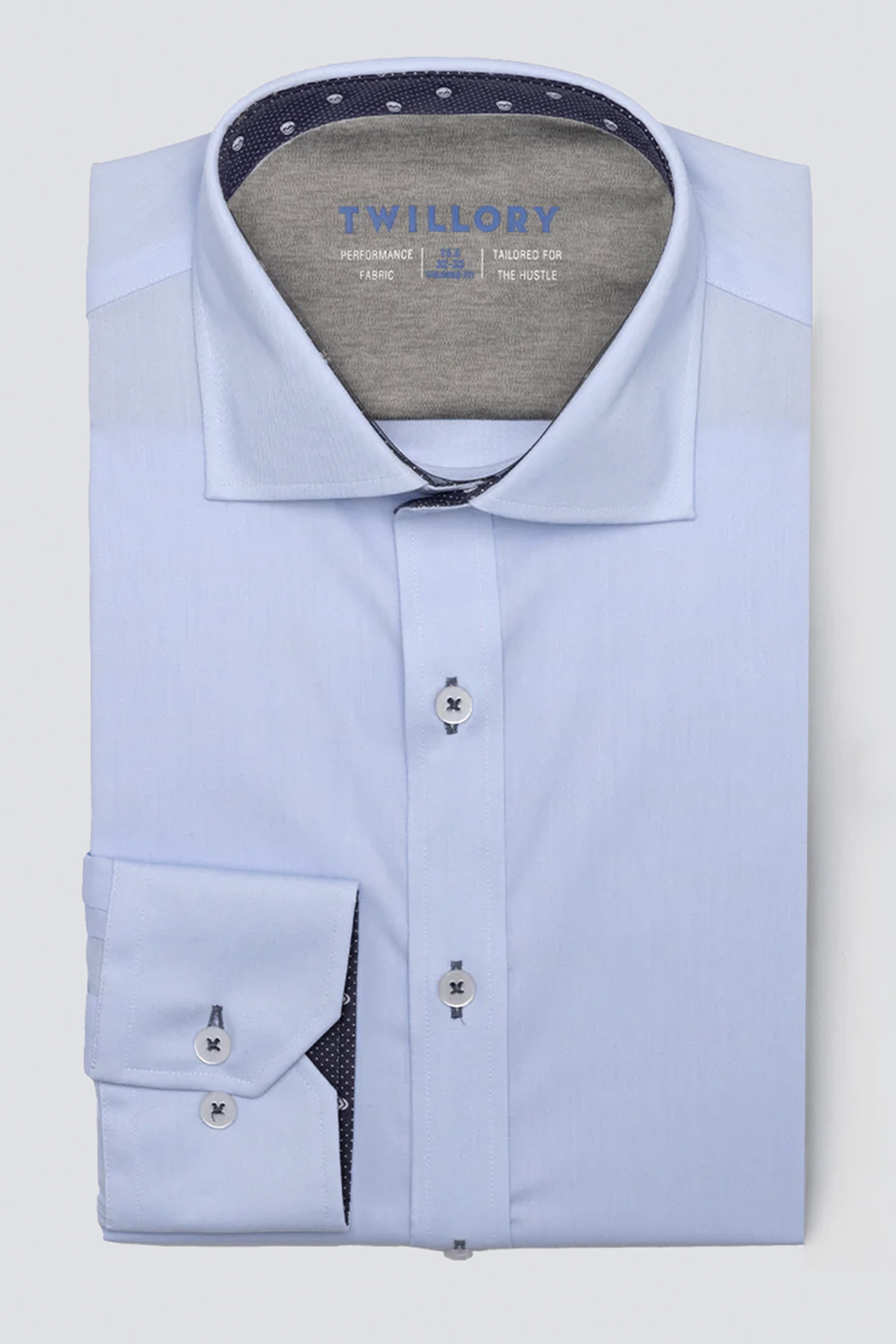 A neatly folded Twillory Leader Contrast // Blue Skull Performance Shirt in light blue with a spread collar, white buttons, dark blue threads, and navy polka dot lining inside the collar/cuffs. Features 4-way stretch and “Twillory” branding on the inner collar.