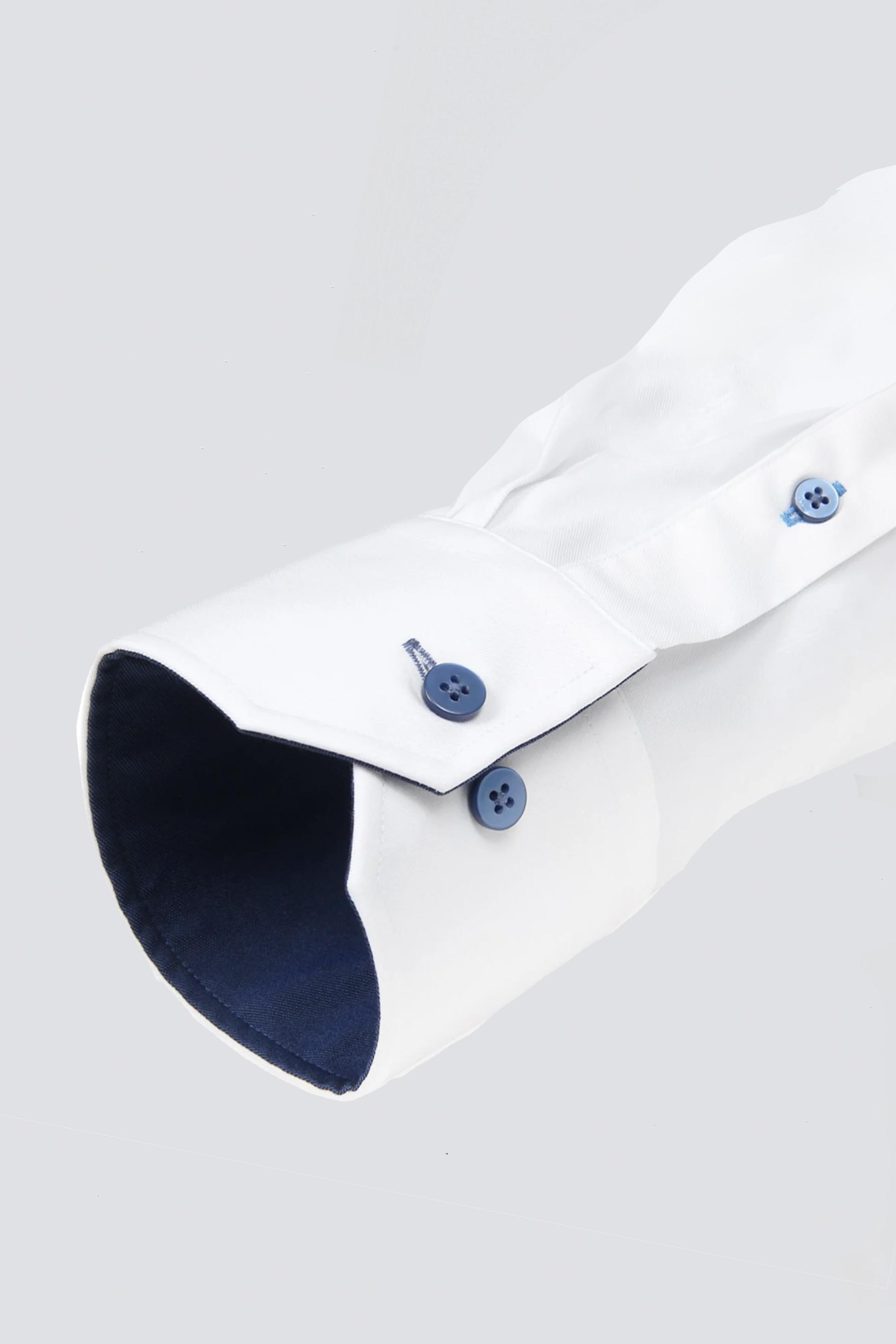 A close-up of the Twillory Leader Contrast // Navy shirt sleeve against a light gray background shows the cuff with two blue buttons, contrasting dark navy inner lining, visible stitching, and 4-way stretch fabric neatly folded.