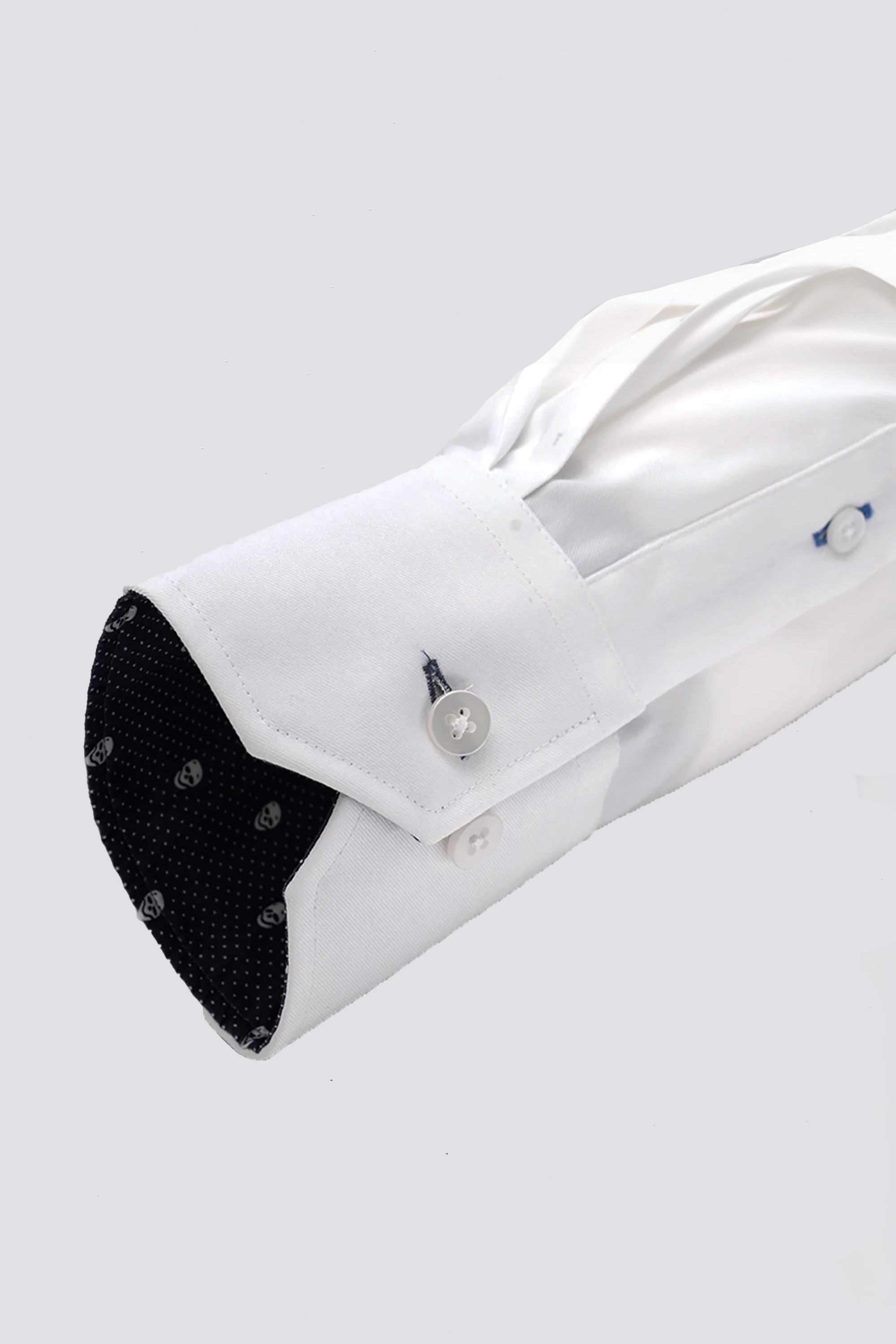 A close-up of Twillory’s Leader Contrast // Navy Skull Performance Shirt cuff with two white buttons. The black inner cuff features white skull dots. The neatly pressed shirt has 4-way stretch, shown against a light gray background.