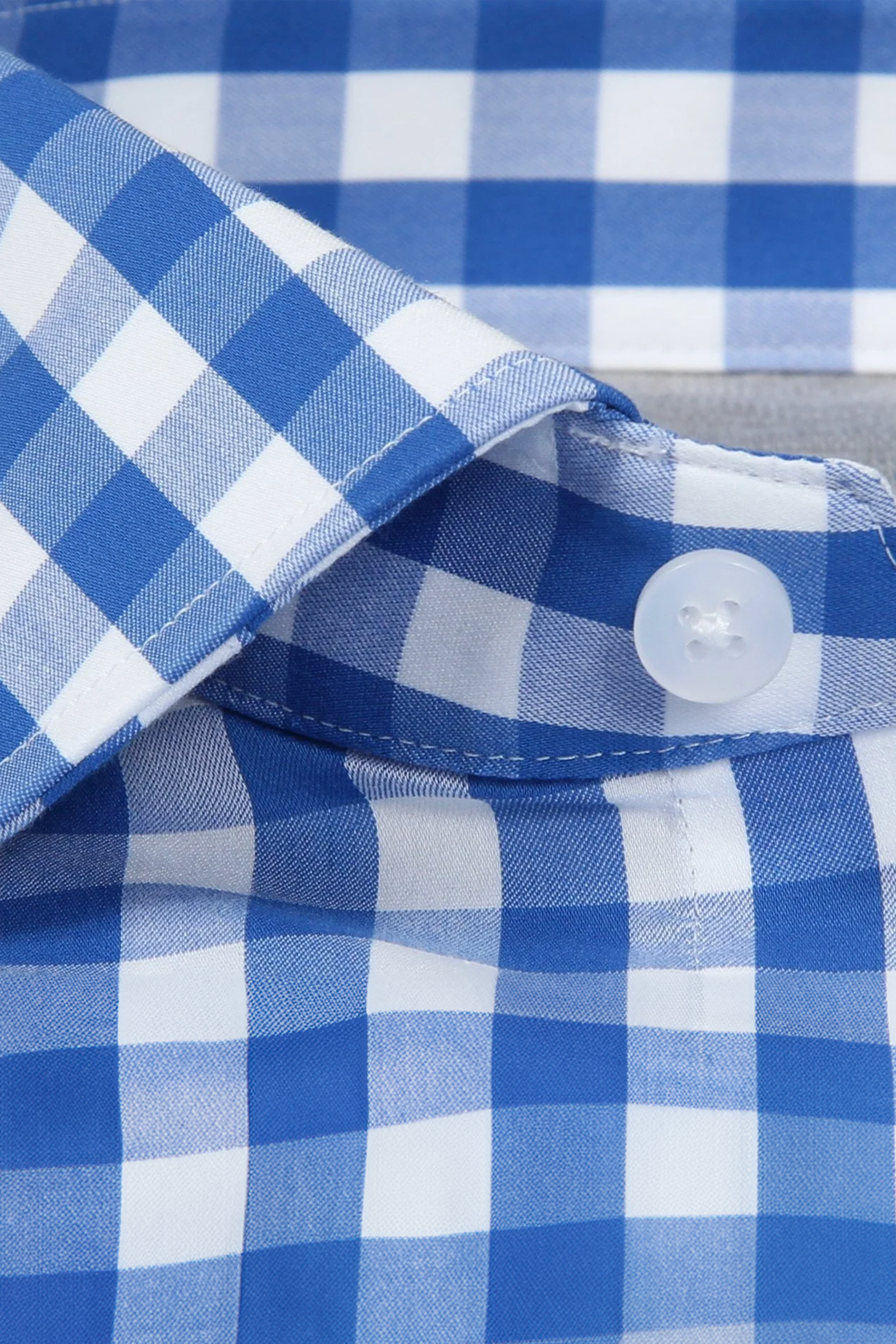 Close-up of the Twillory Leader Gingham // Blue White shirt, featuring a fastened plastic white button by the collar. Its lightweight 4-way stretch fabric offers comfort, visible stitching, texture, and moisture-wicking to keep you dry.
