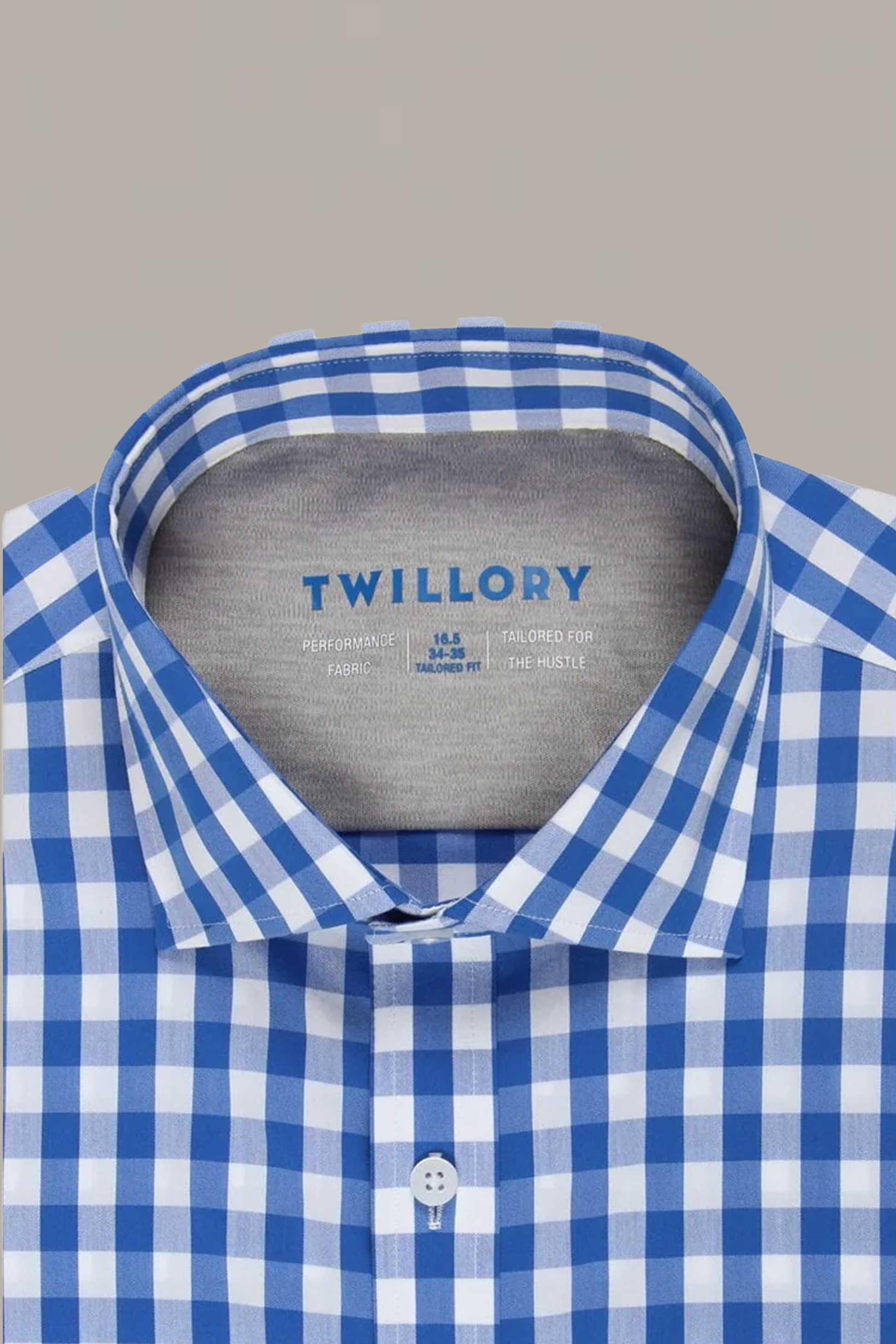 The Twillory Leader Gingham // Blue White shirt, featuring a blue and white check pattern and spread collar, is neatly folded. The label shows sizing, care, and moisture-wicking info. Background: plain light gray.