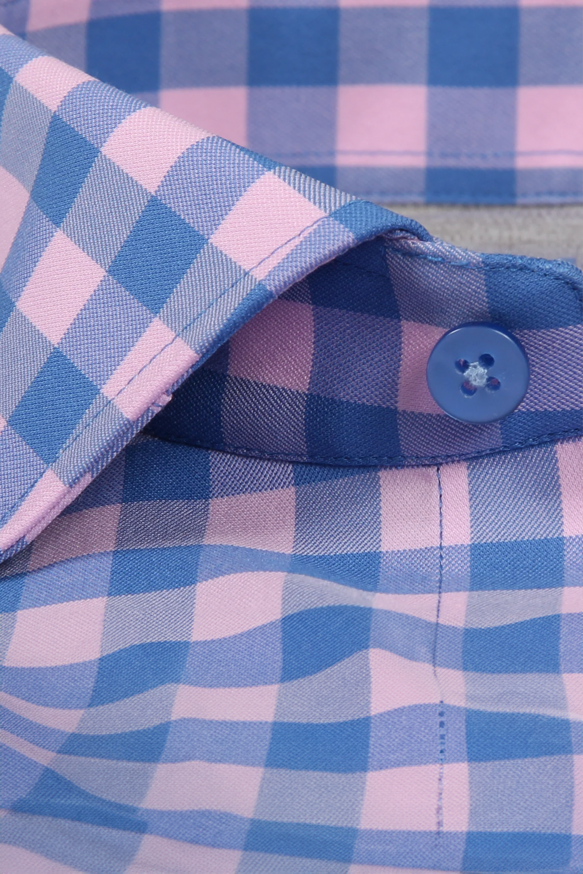 Close-up of the Twillory Leader Gingham // Pink Blue shirt collar, showing its blue and pink check pattern, neat stitching, moisture-wicking fabric, and a blue plastic button near the edge.