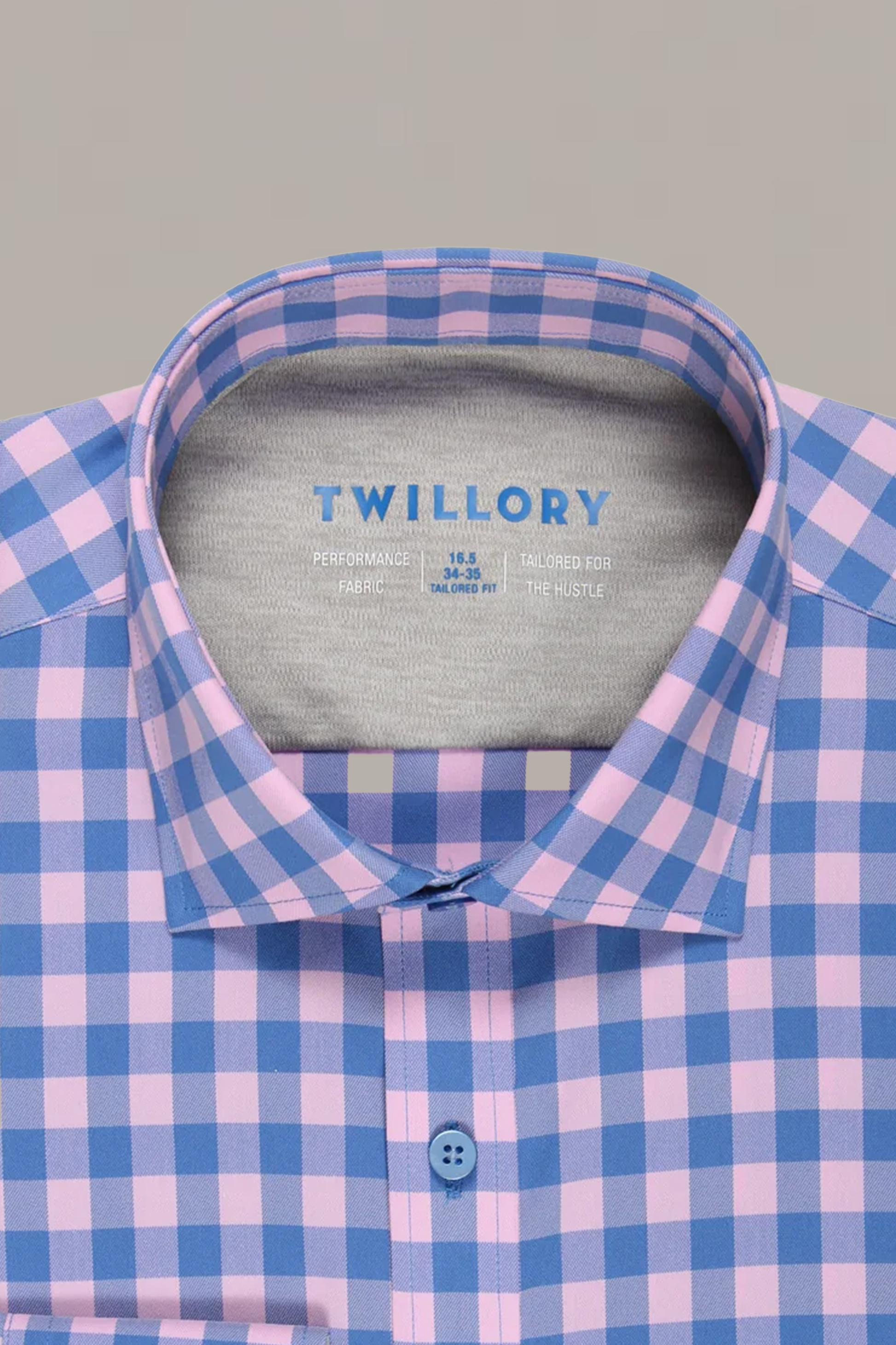 A close-up of Twillory’s Leader Gingham // Pink Blue performance shirt shows a neatly folded collar and blue-printed branding on a light gray background, with a pink and blue check pattern and moisture-wicking technology.
