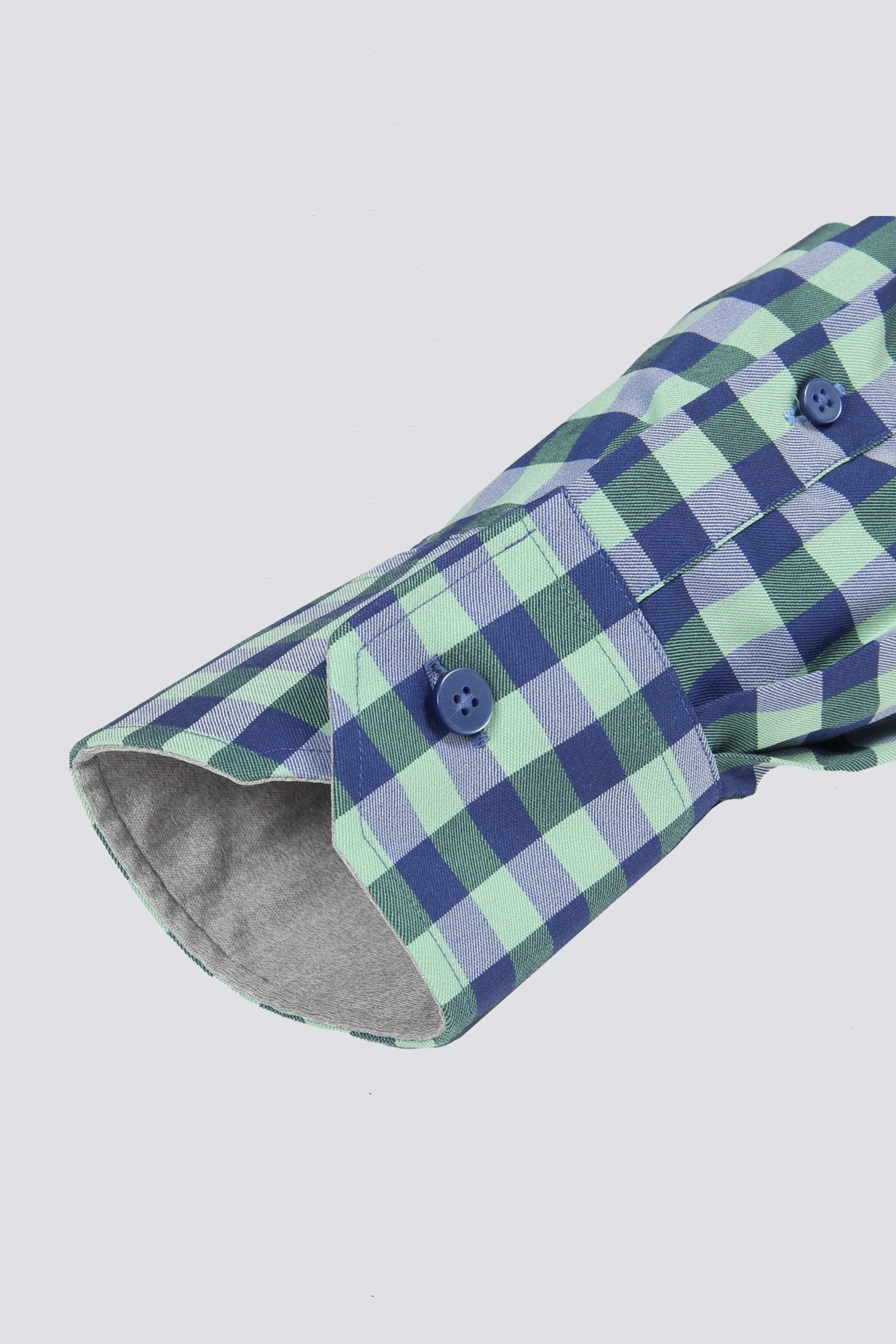 A close-up of the Twillory Leader Gingham // Green Blue Performance Shirt cuff shows its blue buttons, 4-way stretch fabric, and light gray inner lining, all set against a plain white background.